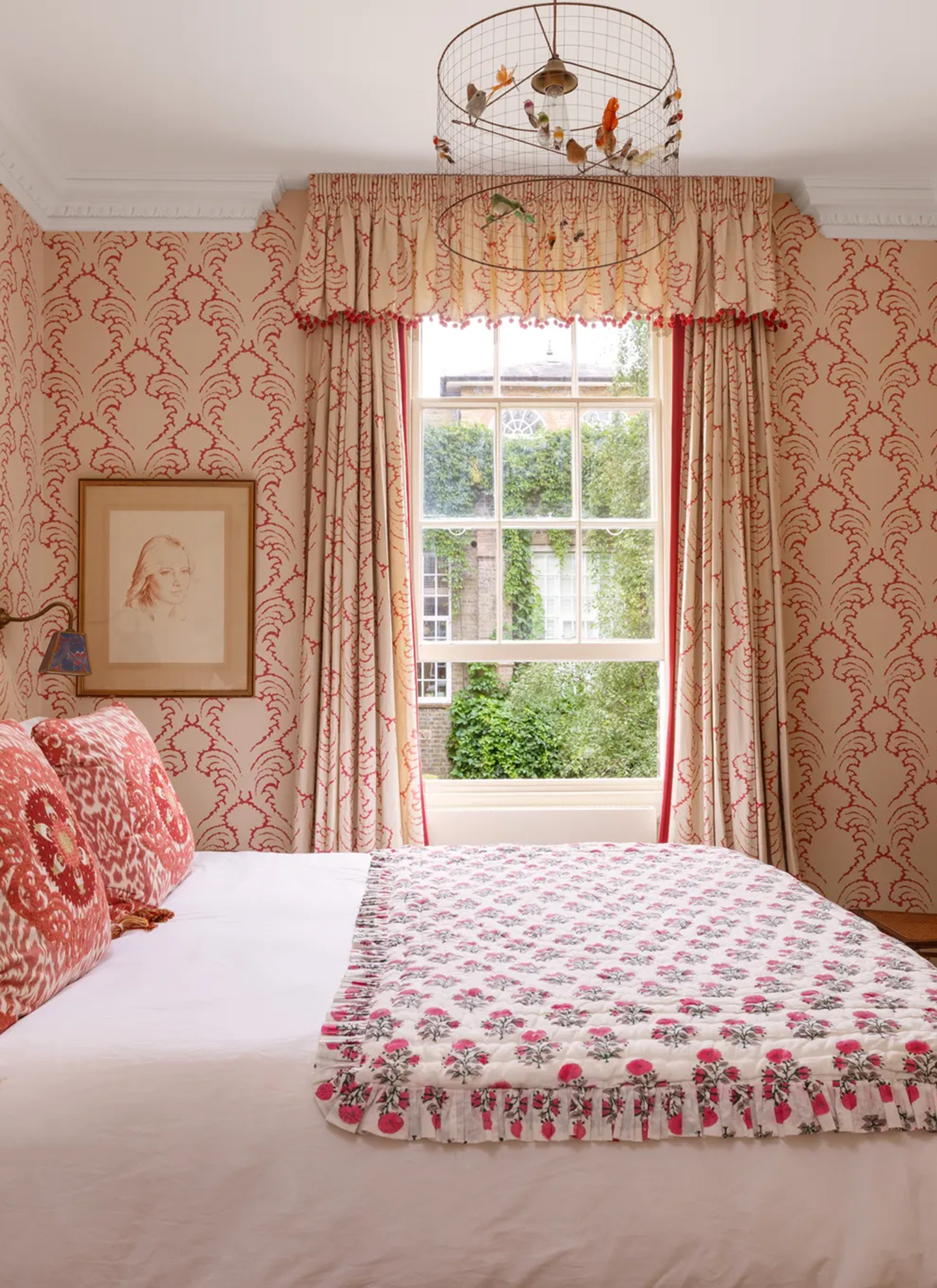 A guest bedroom with pink patterned wallpaper and a delicate wireframe birdcage chandelier with colorful bird figurines hanging from the ceiling