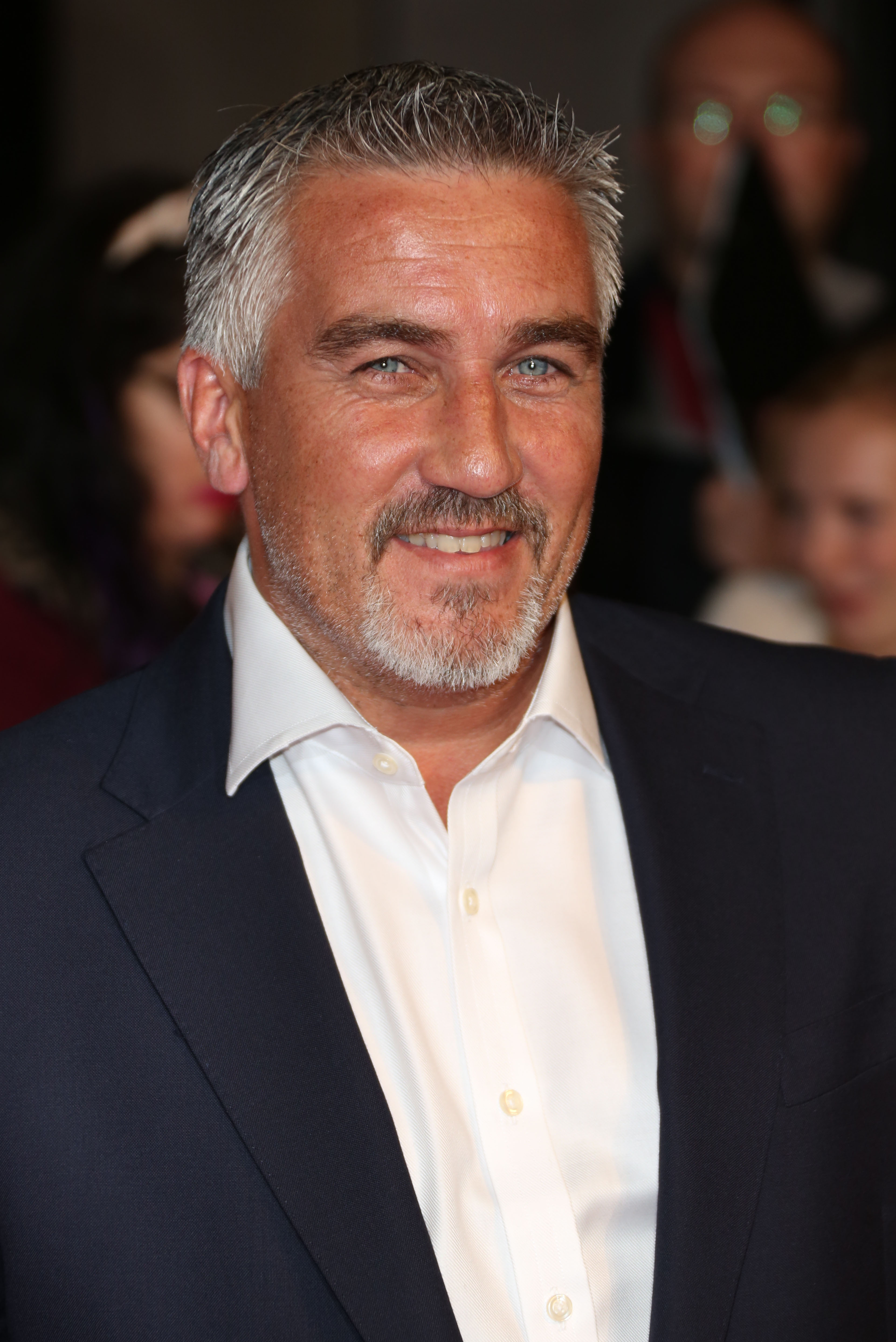 Paul Hollywood pictured smiling wearing a black suit jacket and white shirt