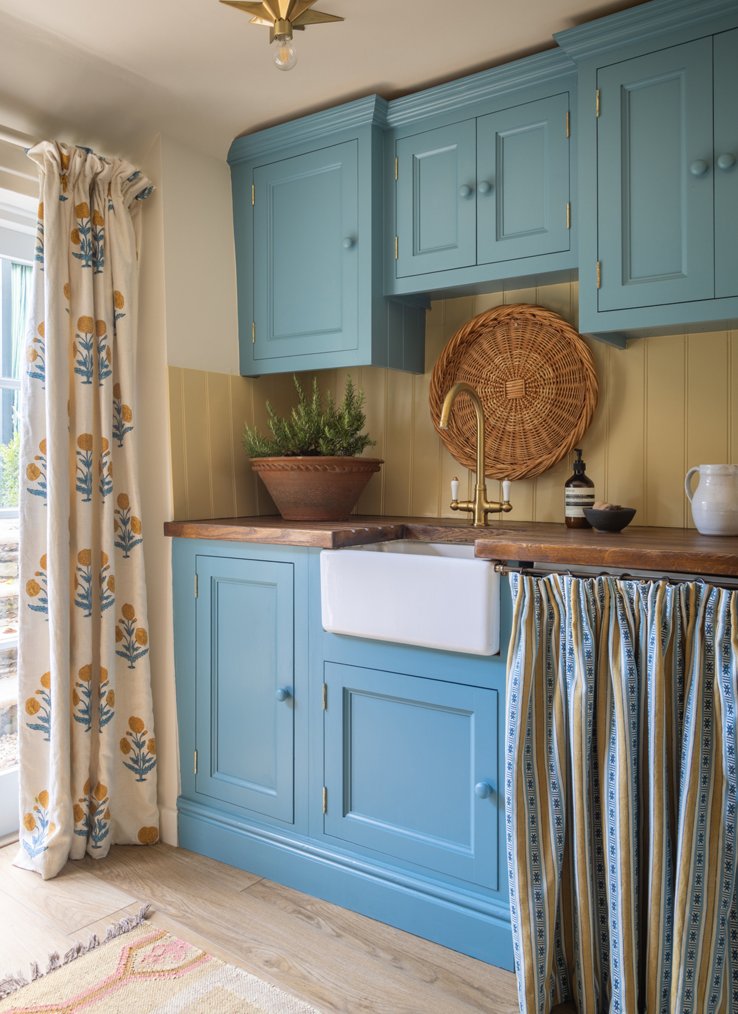 a country kitchen with blue cabinetry and white and yellow floral curtains