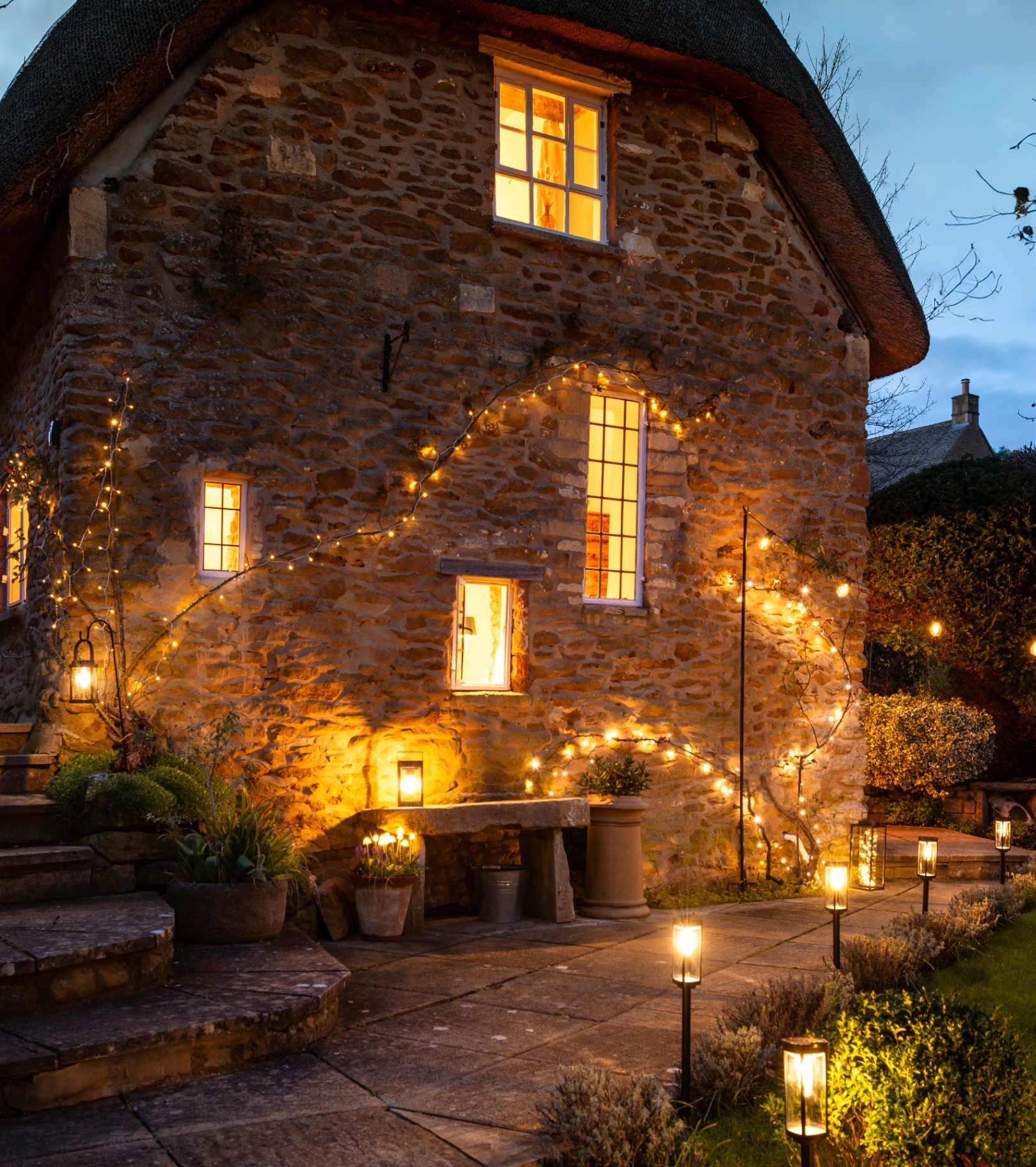 the outside of a stone thatched house covered in solar string lights at night time