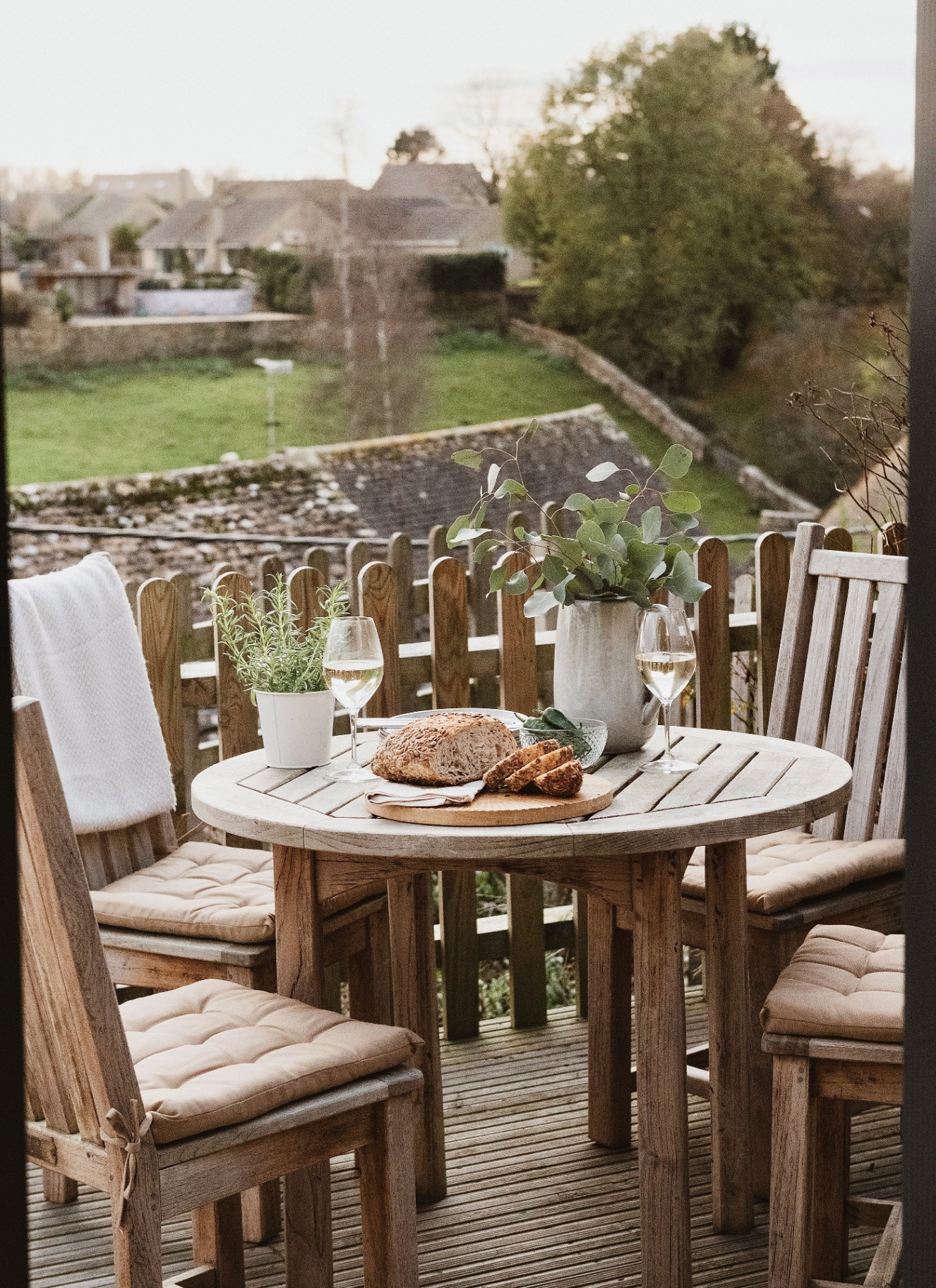 an outdoor seating area with a small wooden dining set on a decking with the cotswolds landscape in the background