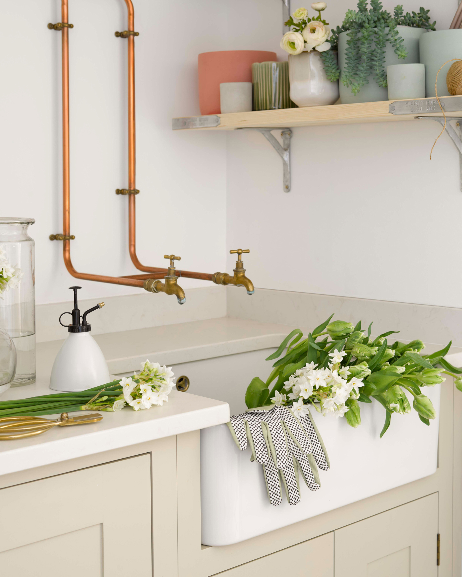 a utility room sink with exposed pipes to the sink, a belfast sink and cut flowers