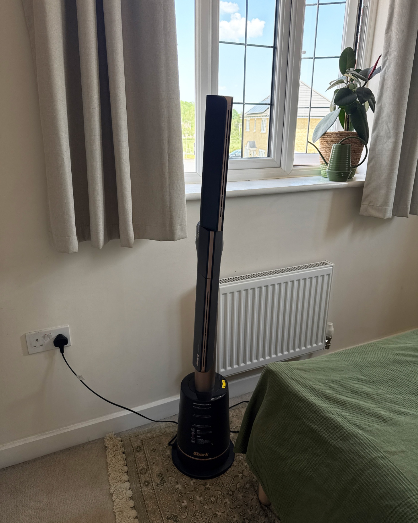 shark turboblade fan at the foot of a bed with a green bedspread in front of a window with grey curtains