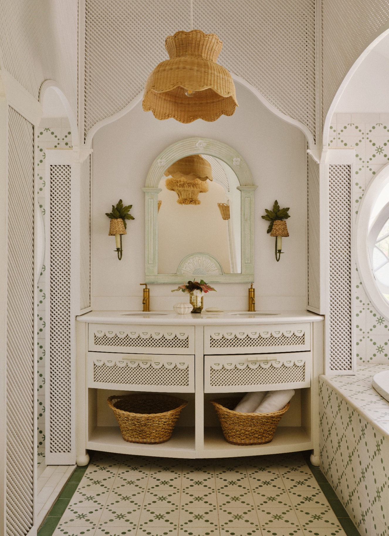 a bathroom with intricate trellis woodwork, a large white vanity with an arched mirror and baskets underneath and a large rattan pendant shade