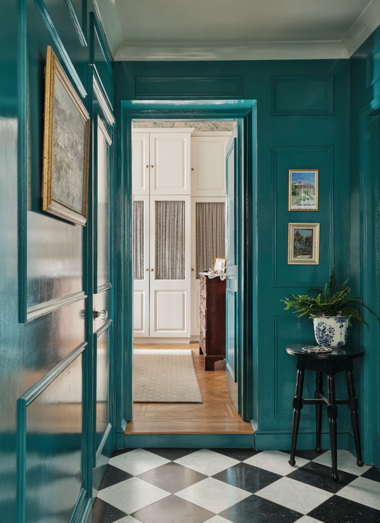 a hallway with glossy peacock green panelled walls and white and black check flooring