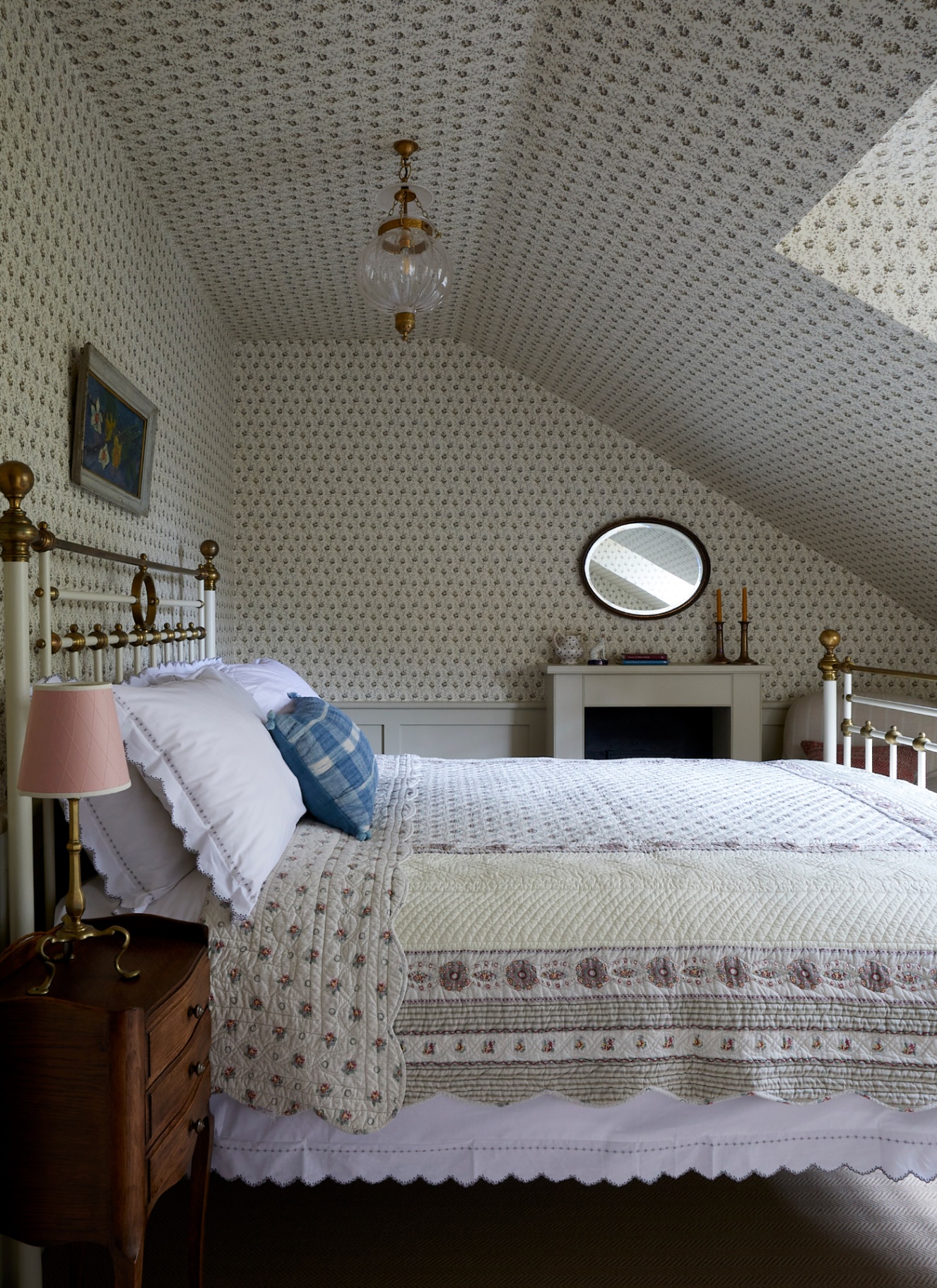 a bedroom with sloping ceiling with white and grey botanical wall paper and an iron bed with a traditional floral bedspread
