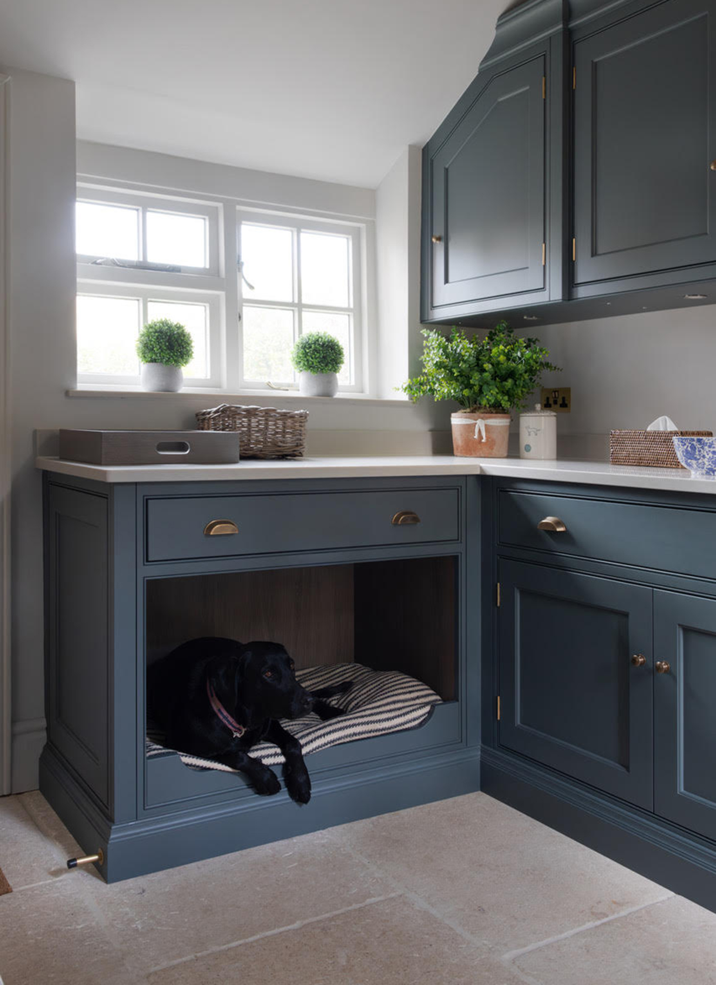 a utility room with navy cabinetry and a dog bed nook under the cabinets with a striped dog bed and a black Labrador inside