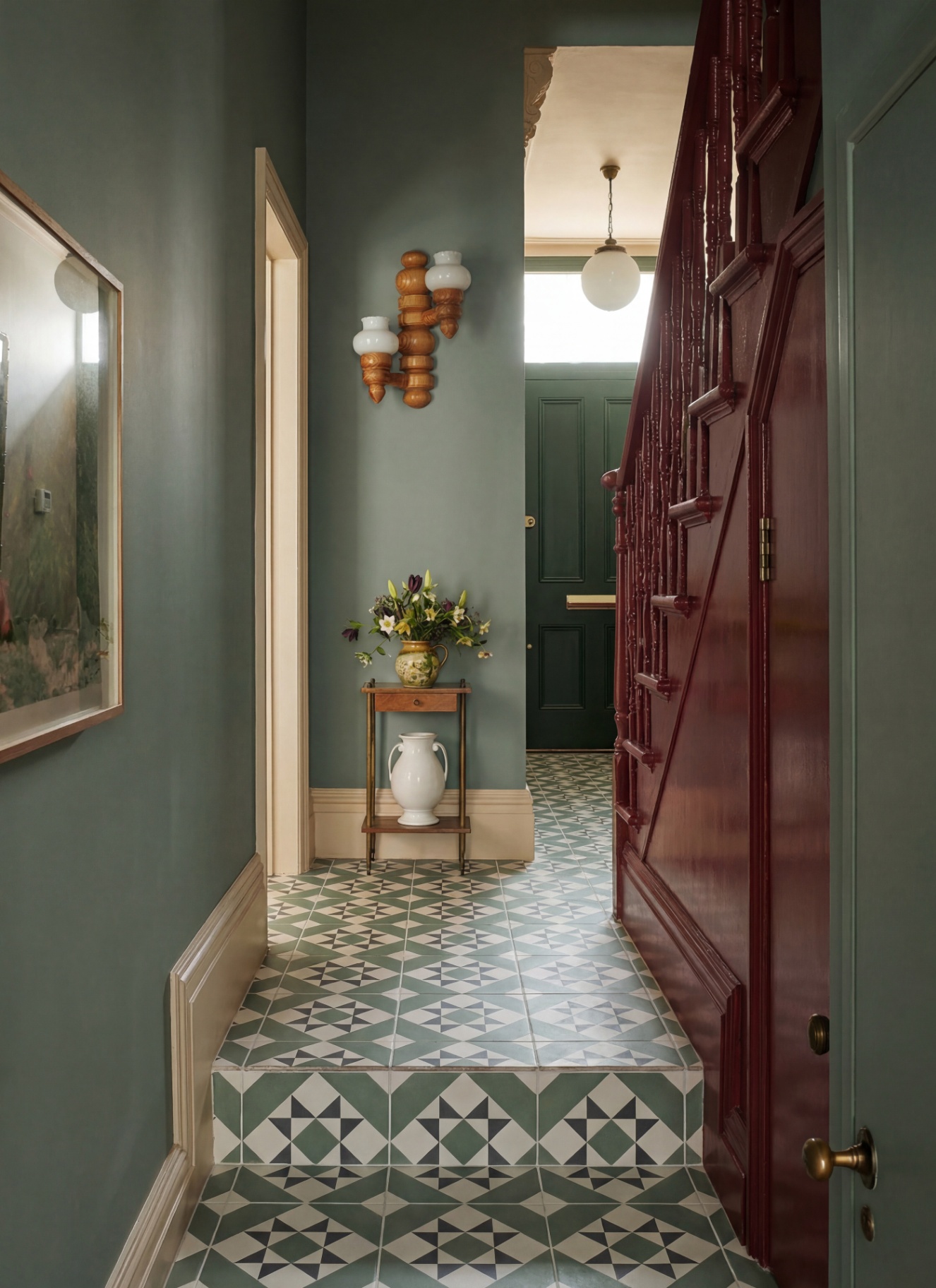 a hallway with green geometric flooring, green walls, glossy red stairs and a wooden sculptural wall light