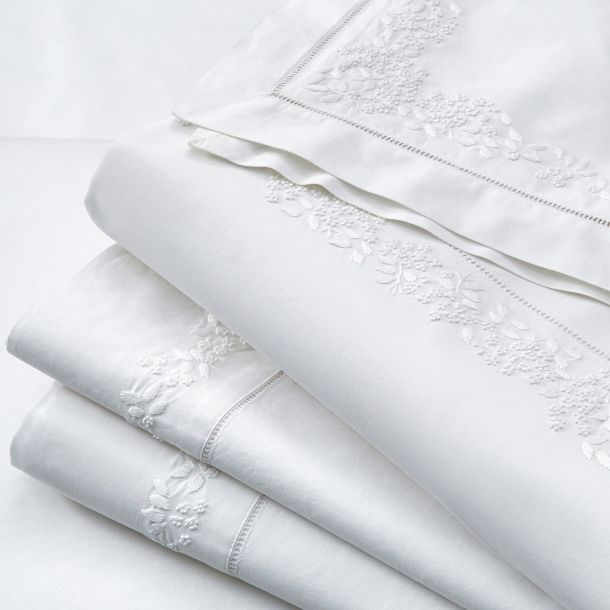a folded white flat sheet with floral border embroidery