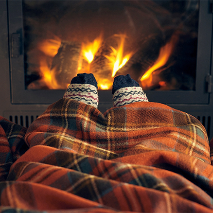 a red tartan blanket covers someone legs next to a roaring fire