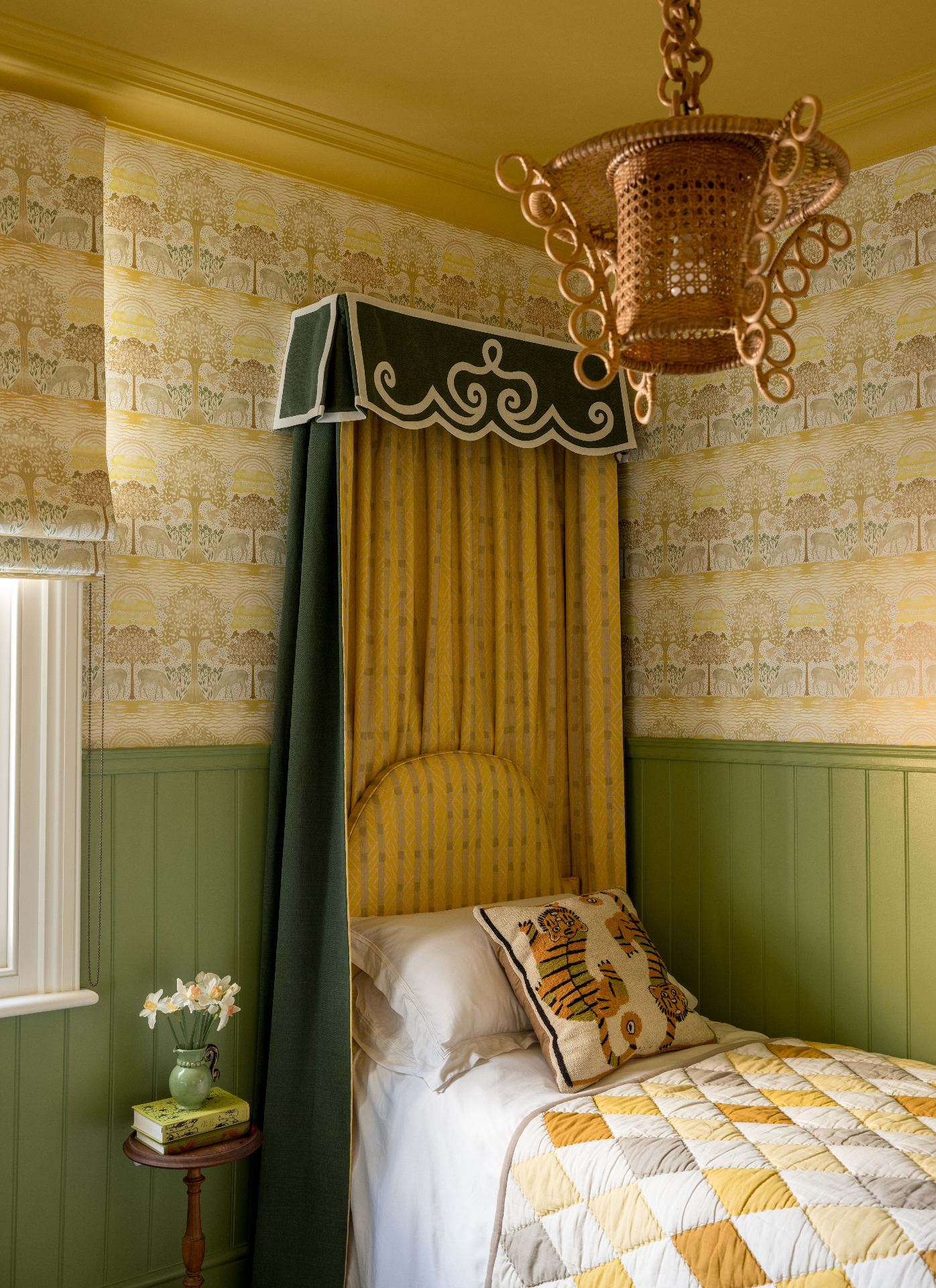 a bedroom with a single bed with a green and yellow canopy, half of the wall with green panelling, half of the wall with yellow patterned wallpaper, a yellow ceiling and a large rattan pendant light