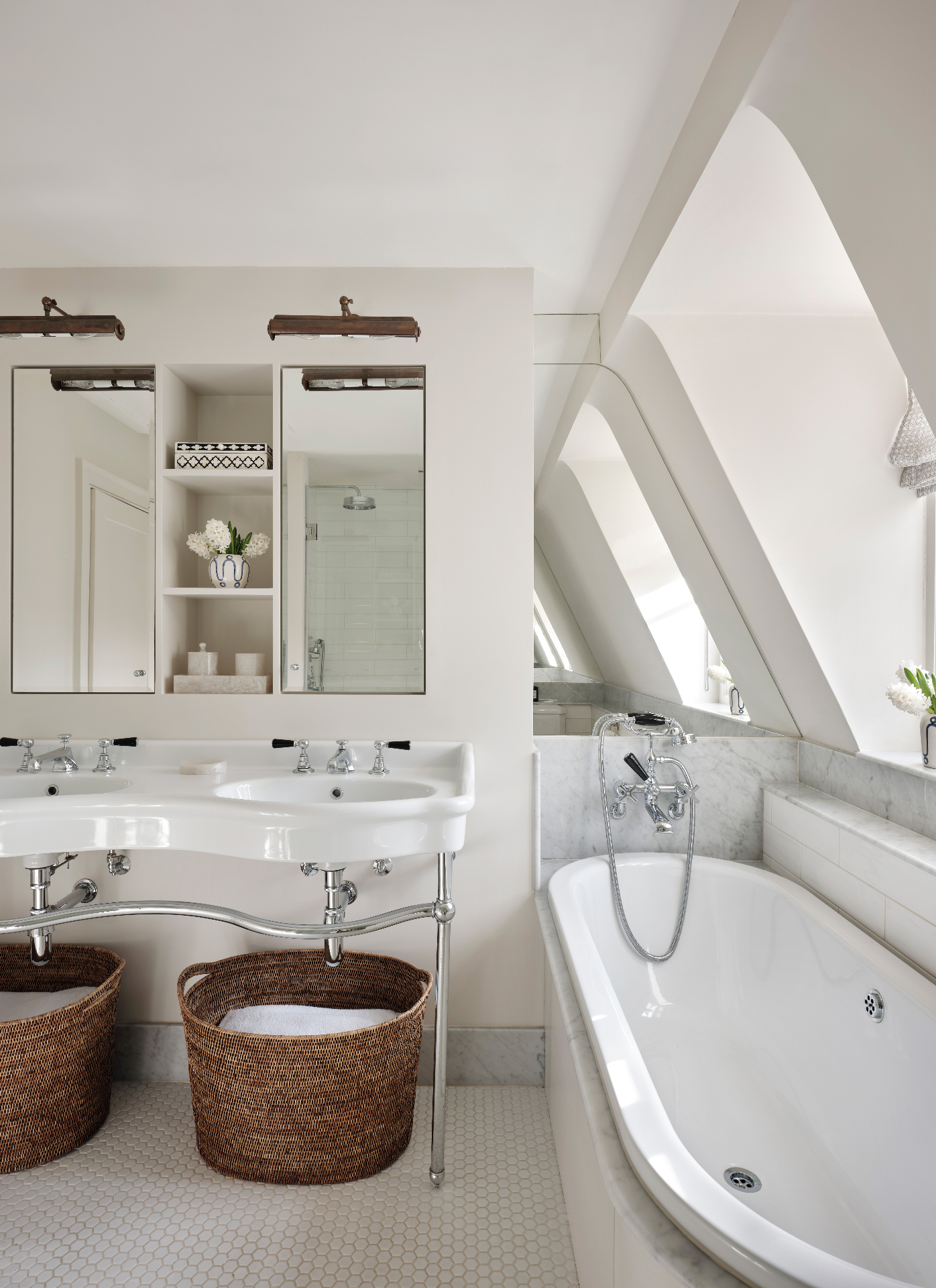 a white bathroom with a double sink, two rectangular mirrors, two brown woven laundry baskets under the sink and a bath tub under the window