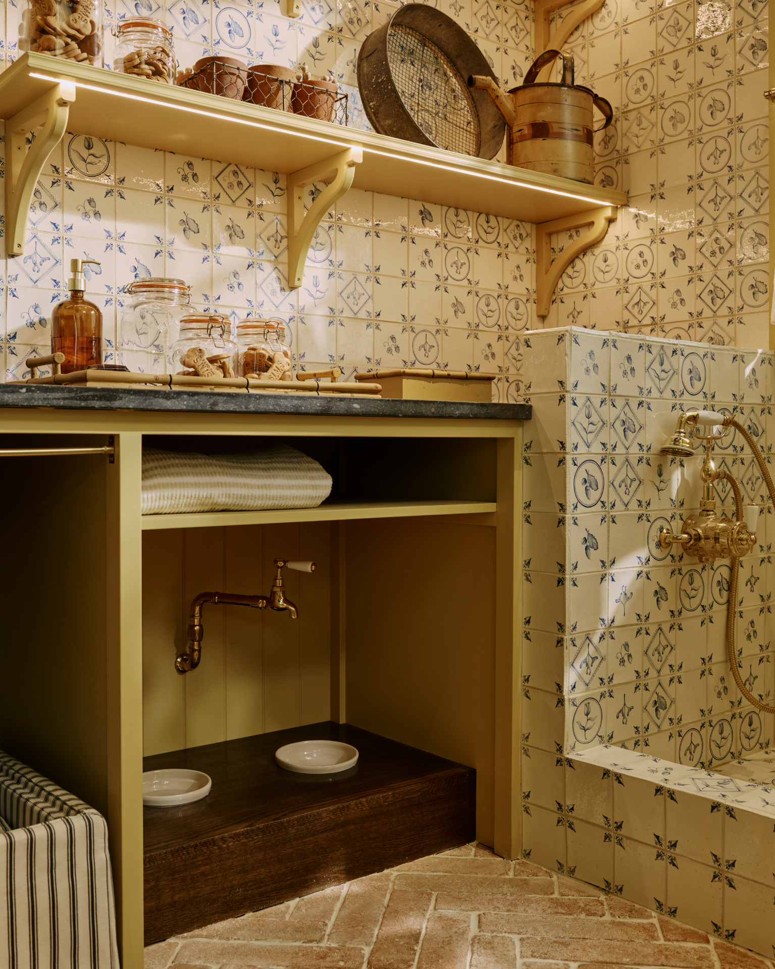 A UTILITY ROOM with a built in wooden dog feeding station, a shower corner with delft tiles and open shelving with dog treats and jars