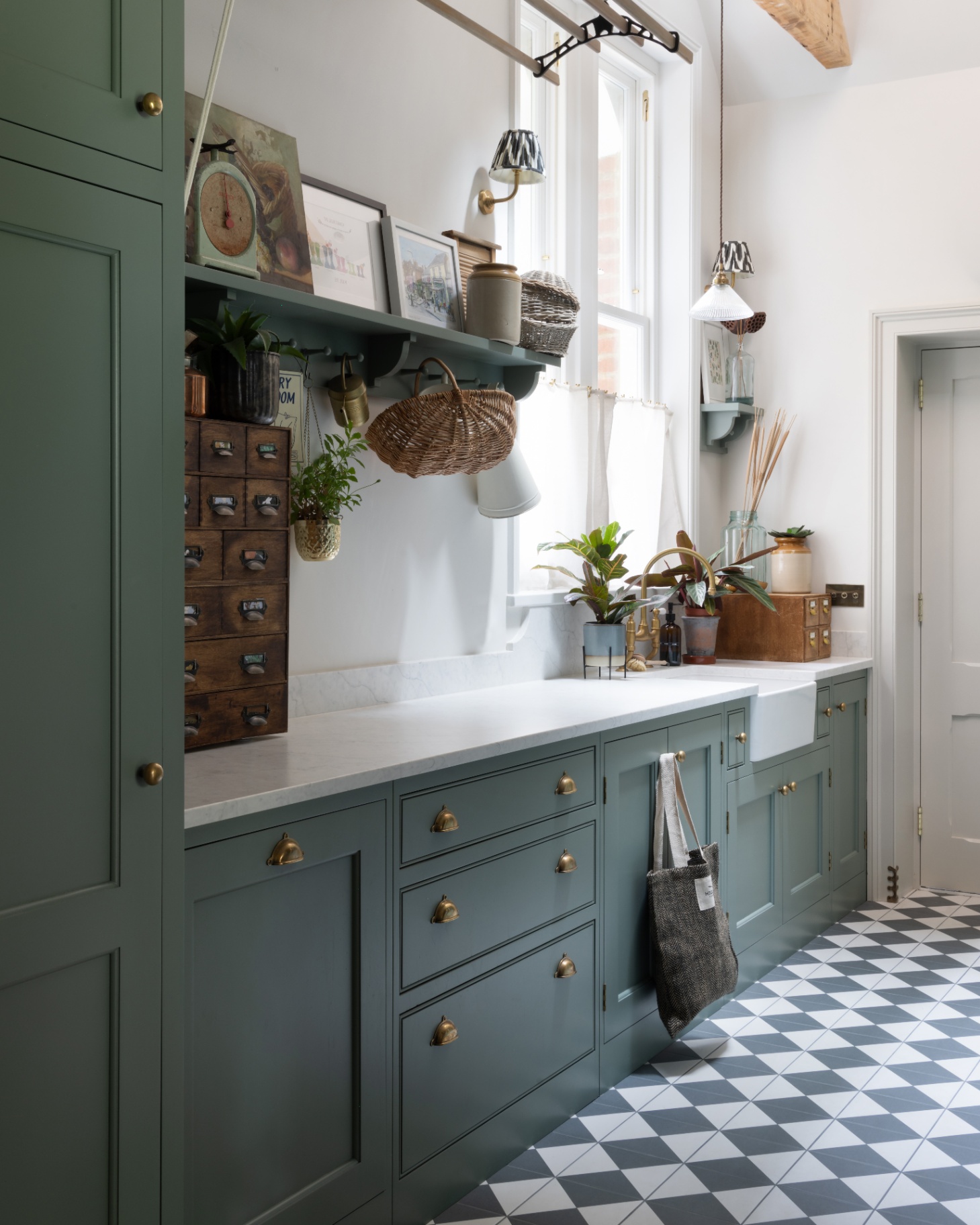 a utility room with black and white checkered flooring and teal green painted cabinets with brass hardware