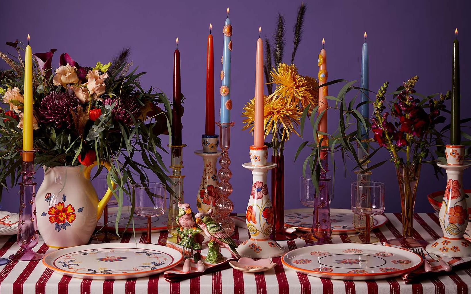 a close up of a table filled with different coloured candle stick, floral vases and candle stick holders and flowers