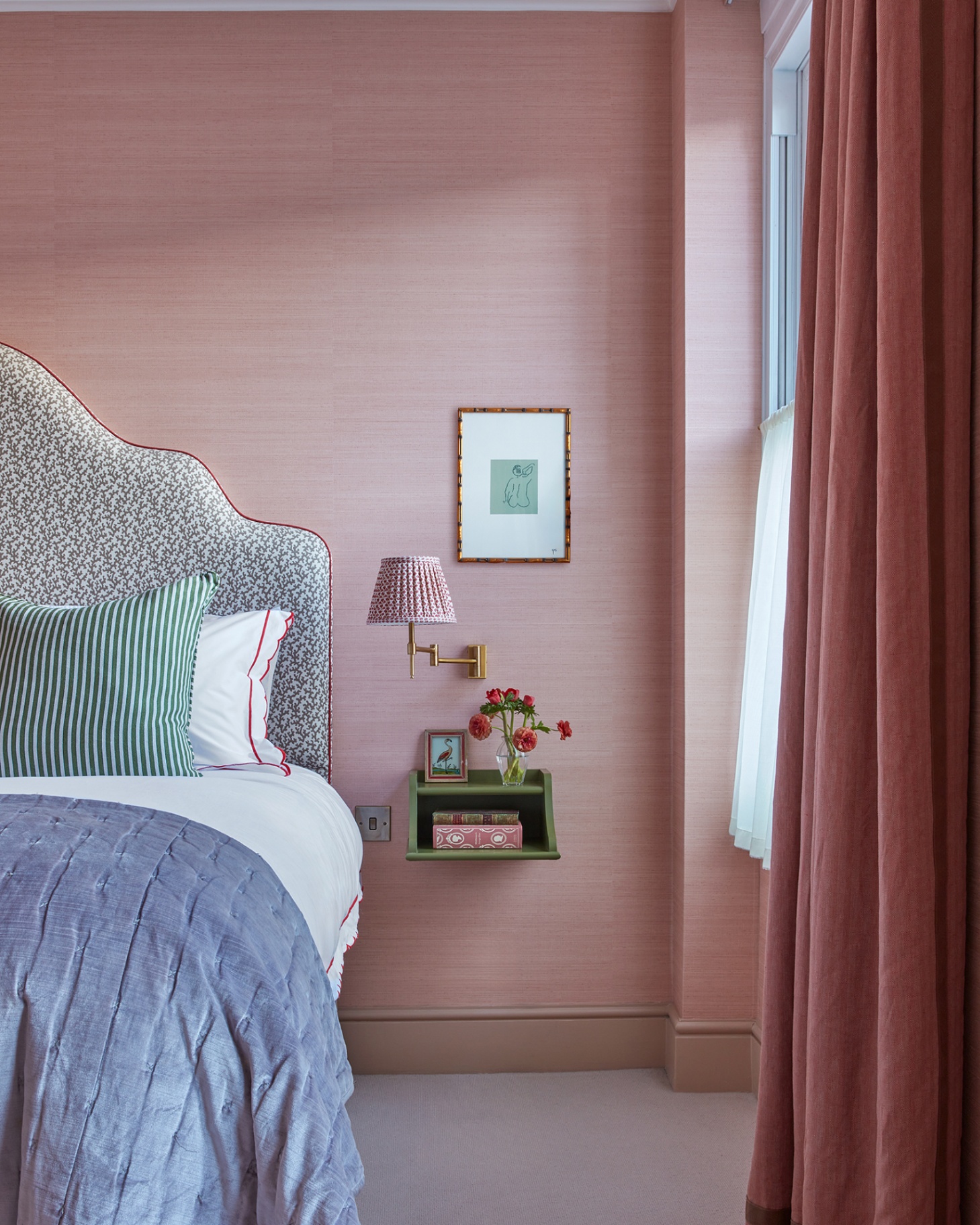 a bedroom with pink walls, a green floating bedside table with a vase of red flowers on it and a reading light above it