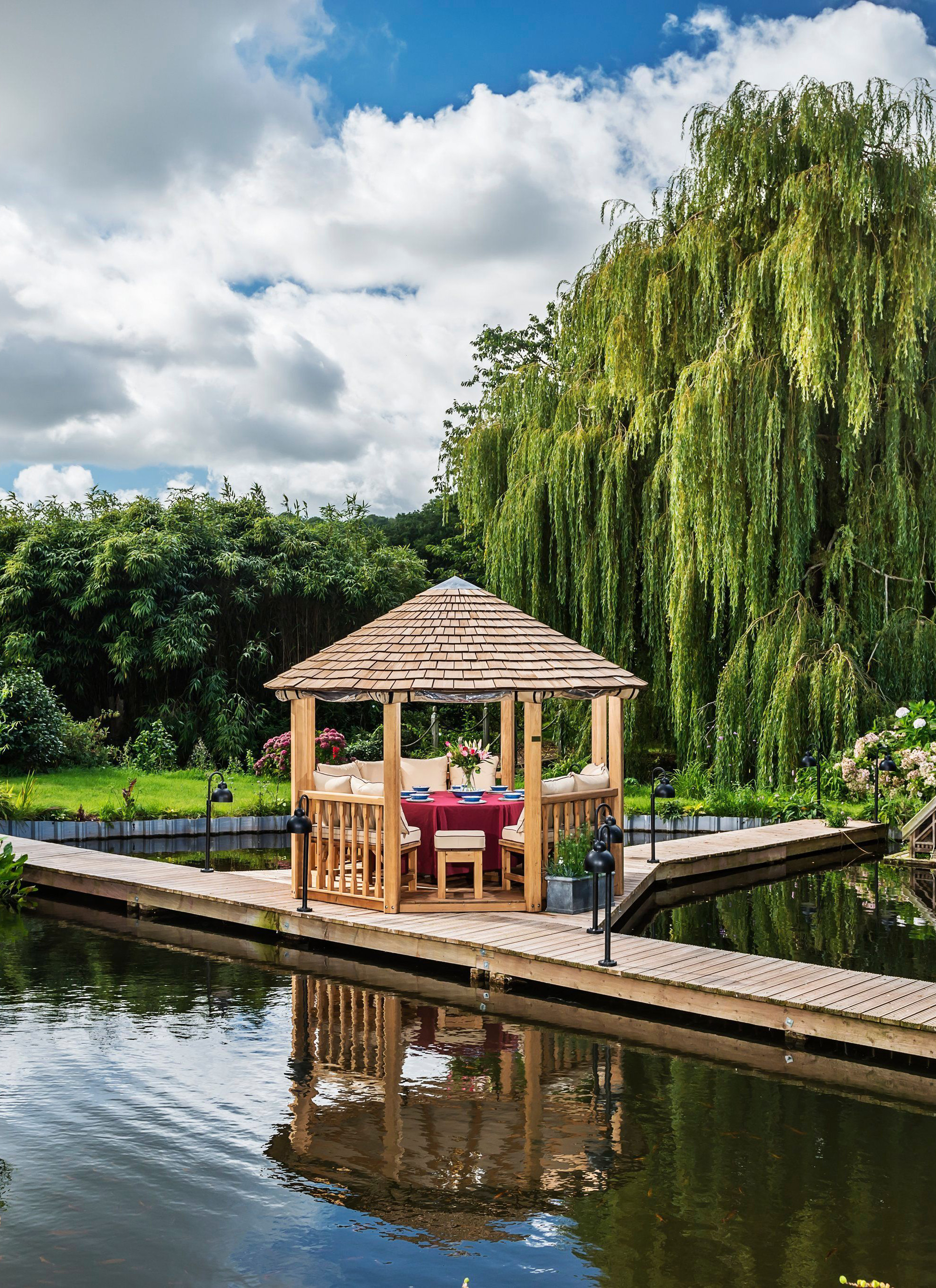 a small circular wooden summer house on a boardwalk over the water surrounded by trees