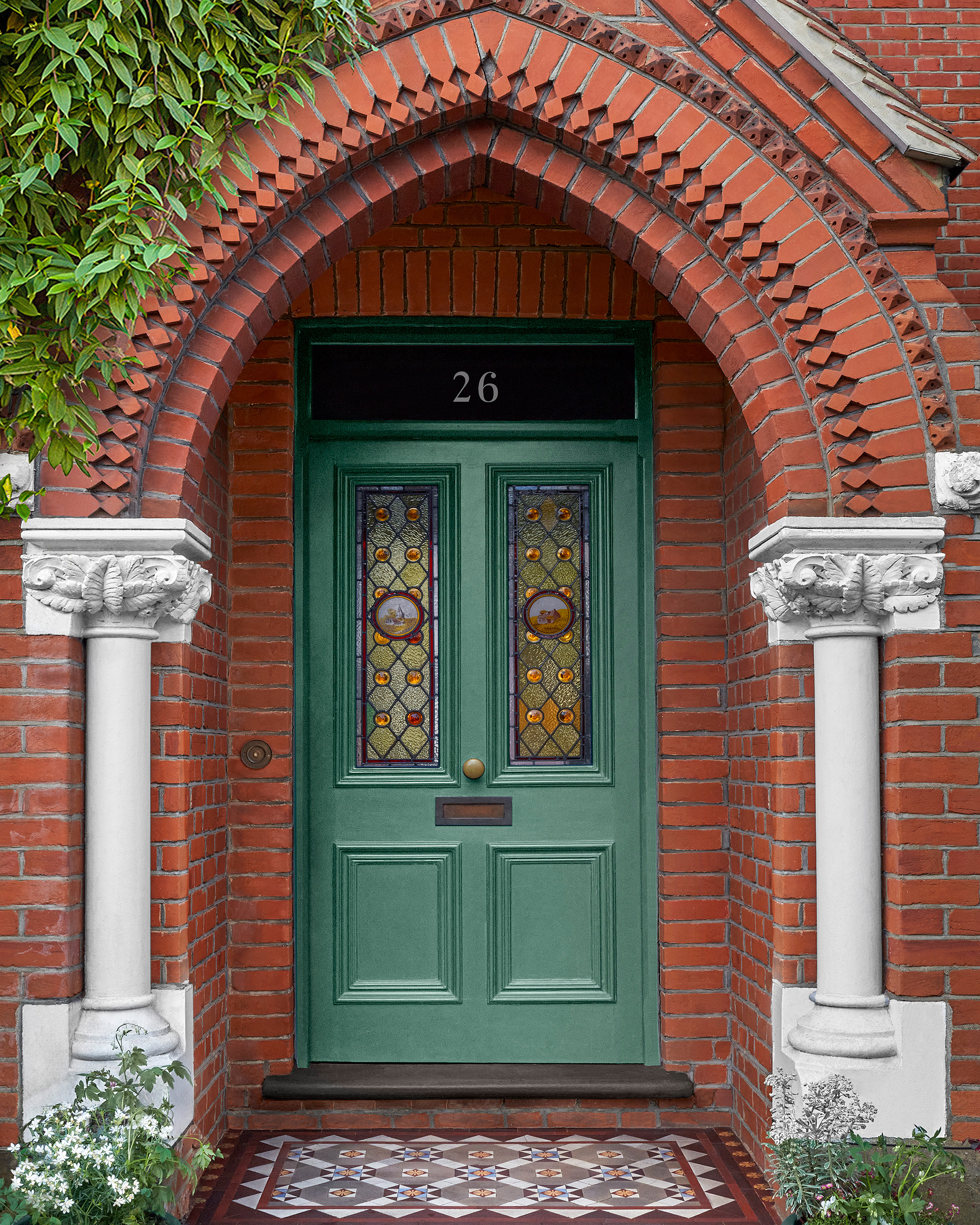 a green front door in a red brick arched porch with a patterned tile floor in front
