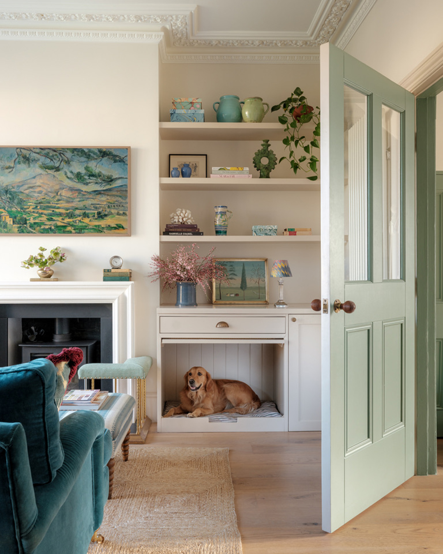 a living room with a sage green open door, a jute rug under a striped ottoman and teal sofa and a build in dog bed alcove with shelving above it