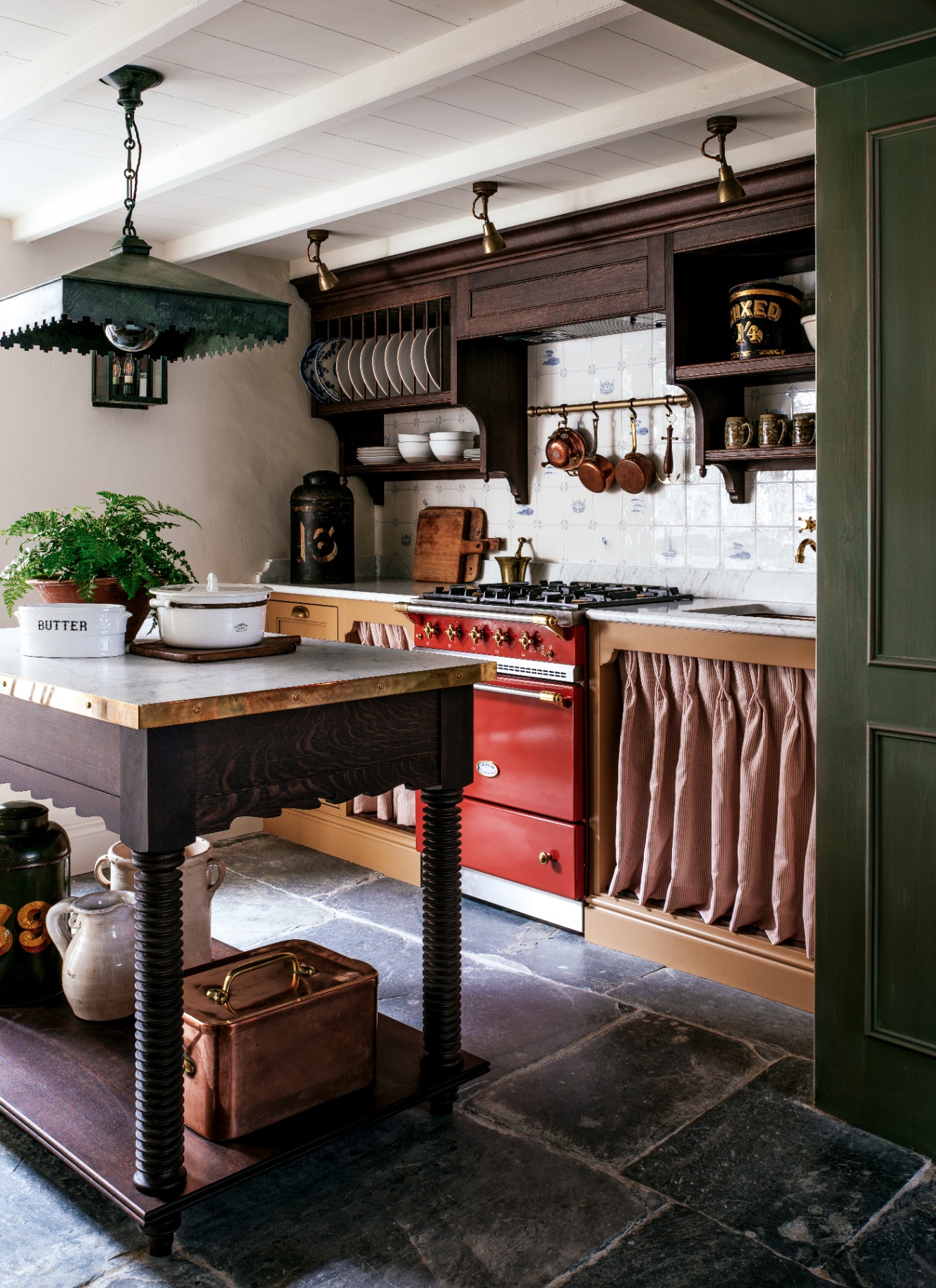 a country kitchen with dark flagstone floors, a large wooden butchers block, a red aga and a dark timber shelf surrounding the cooker