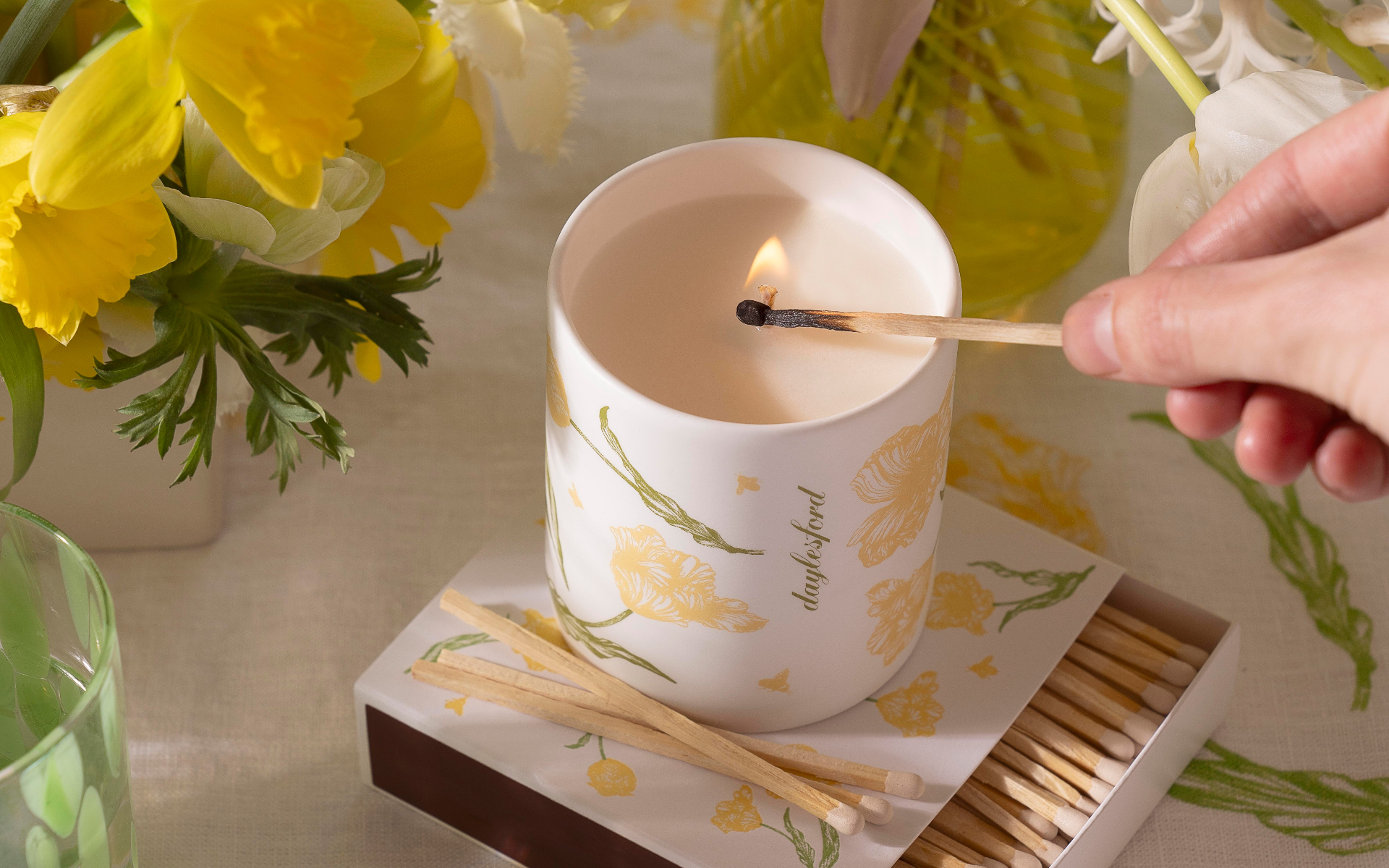 daylesford white candle with yellow flower illustration, with a hand holding 