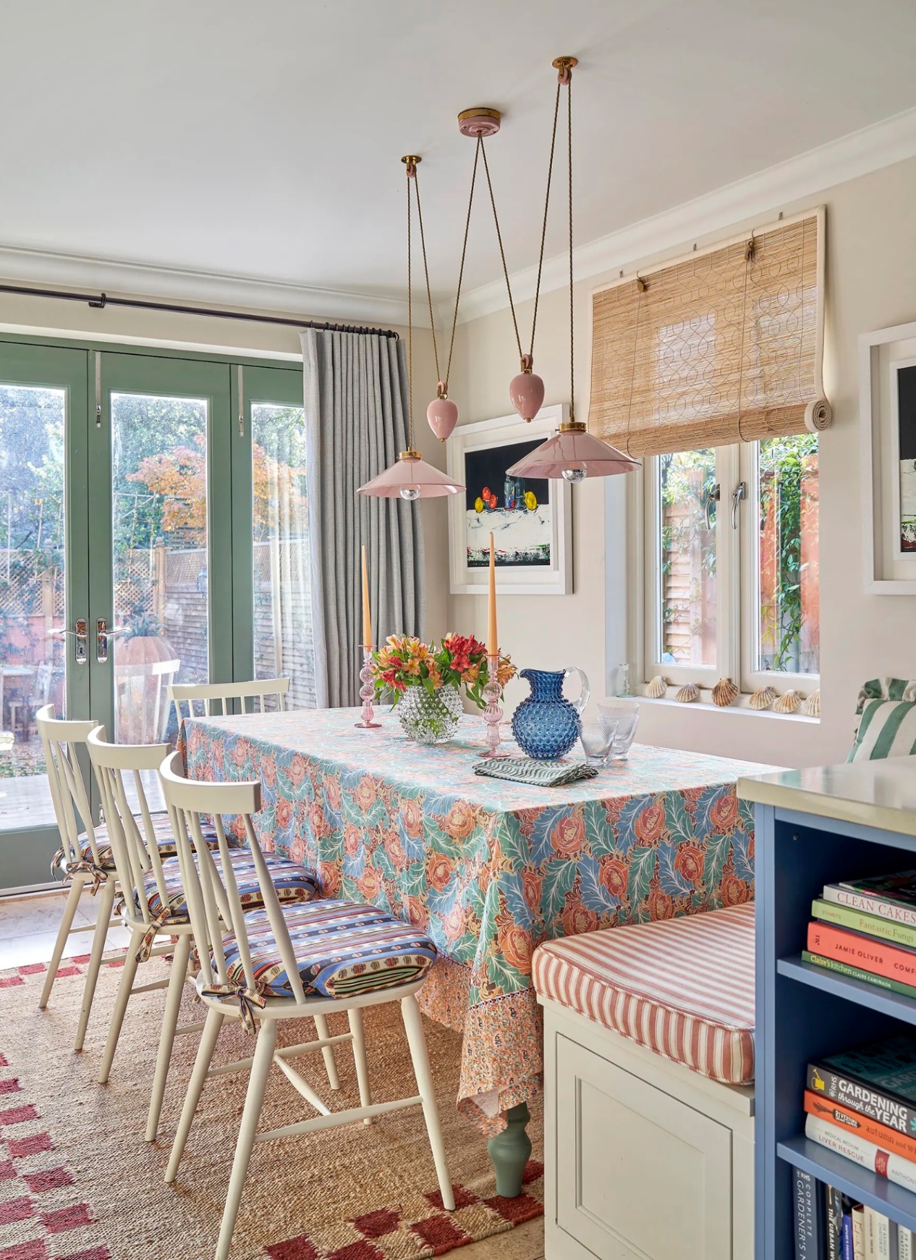 Kitchen dining space featuring a patterned tablecloth, a bench seat, and three pastel pink swagged pendant lights on ceiling hooks.