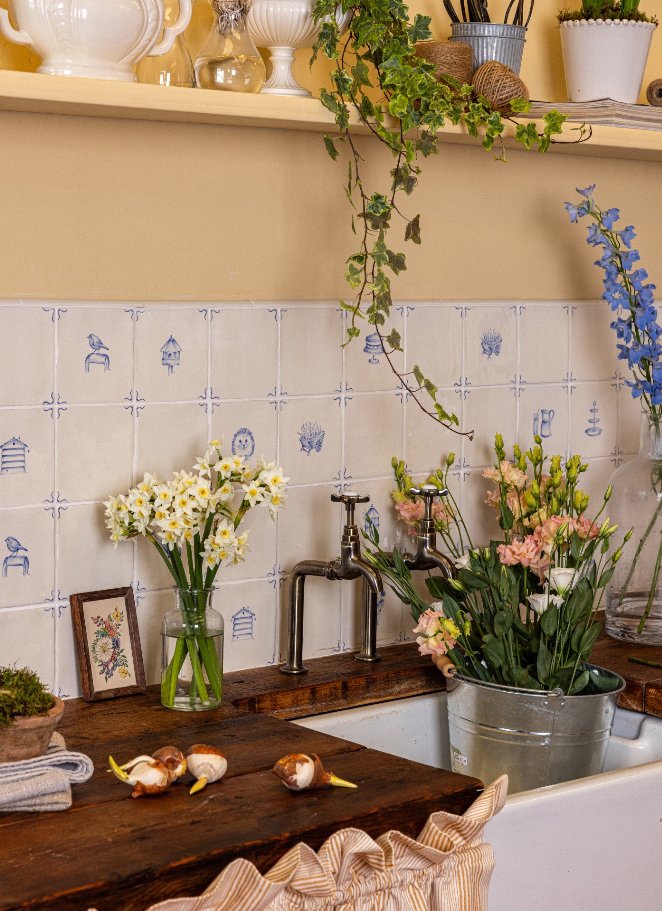 a close up of a utility room sink with a blue and white delt tile splashback and a silver bucket in the sink full of flowers