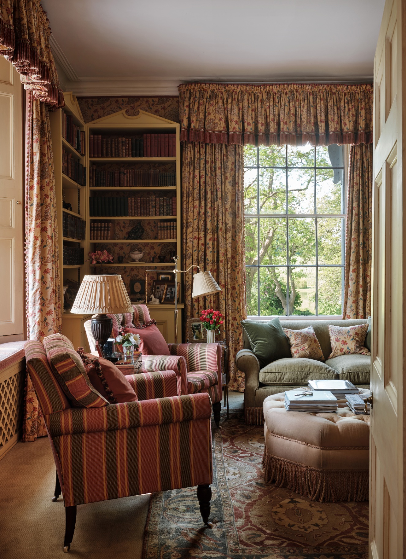  grand living room in warm earthy colours, two striped armchairs, asafe green sofa and a tall white bookcase