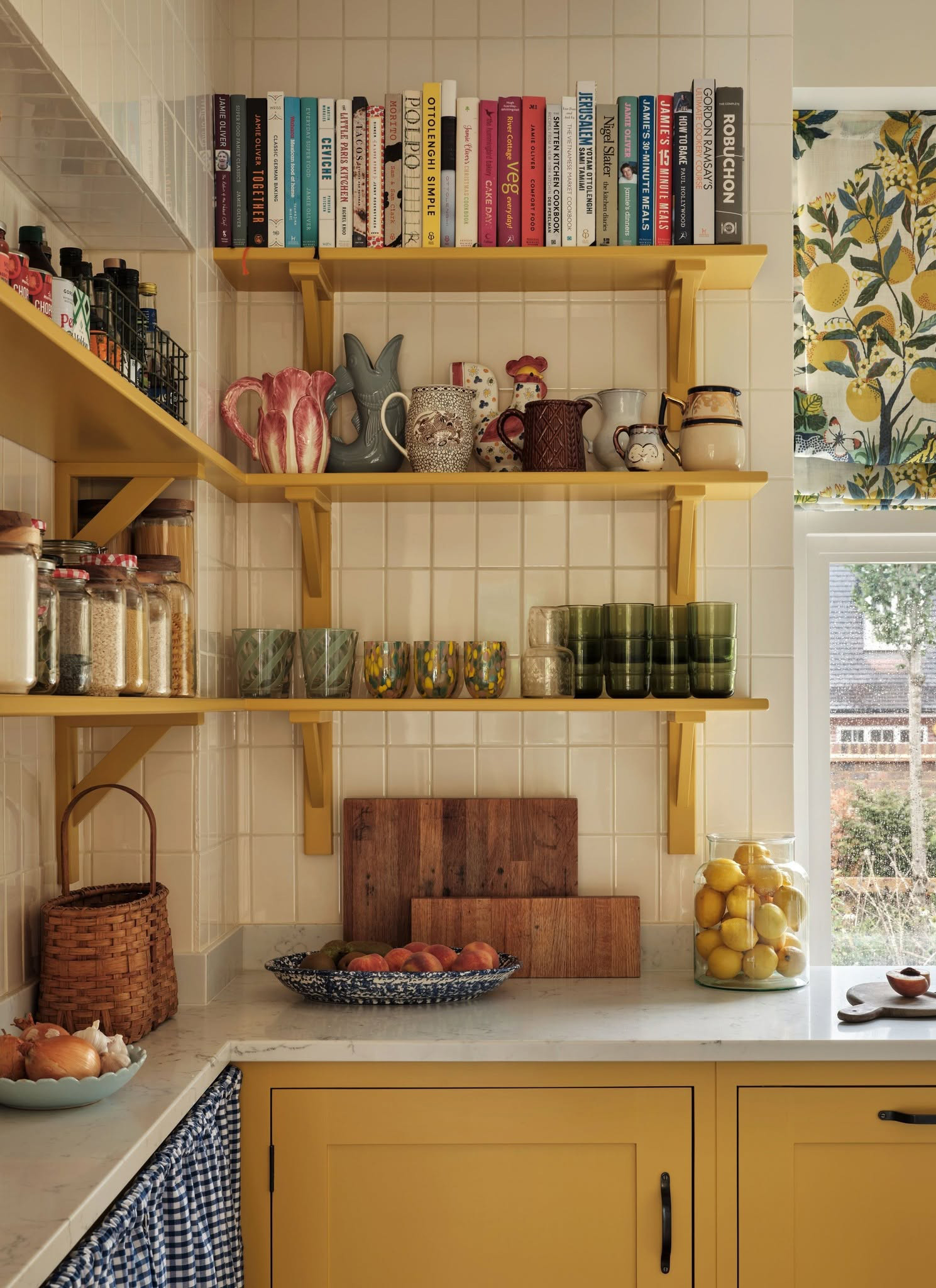 a kitchen corner with yellow cabinets and yellow open shelves with colourful cookbooks and vases