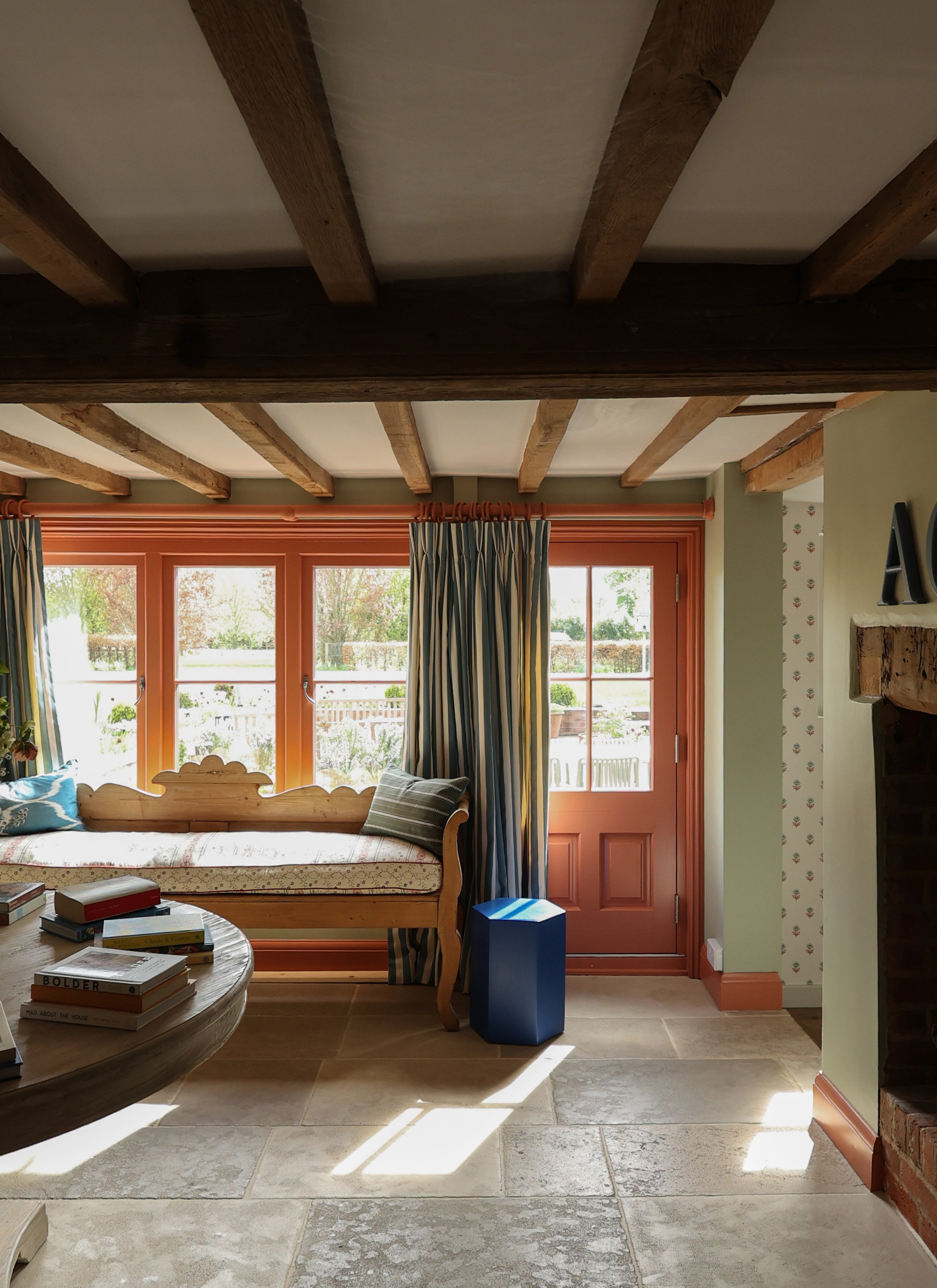 an entrance hall with wooden beams on the ceiling, coral painted door and windows and a window seat with cushions