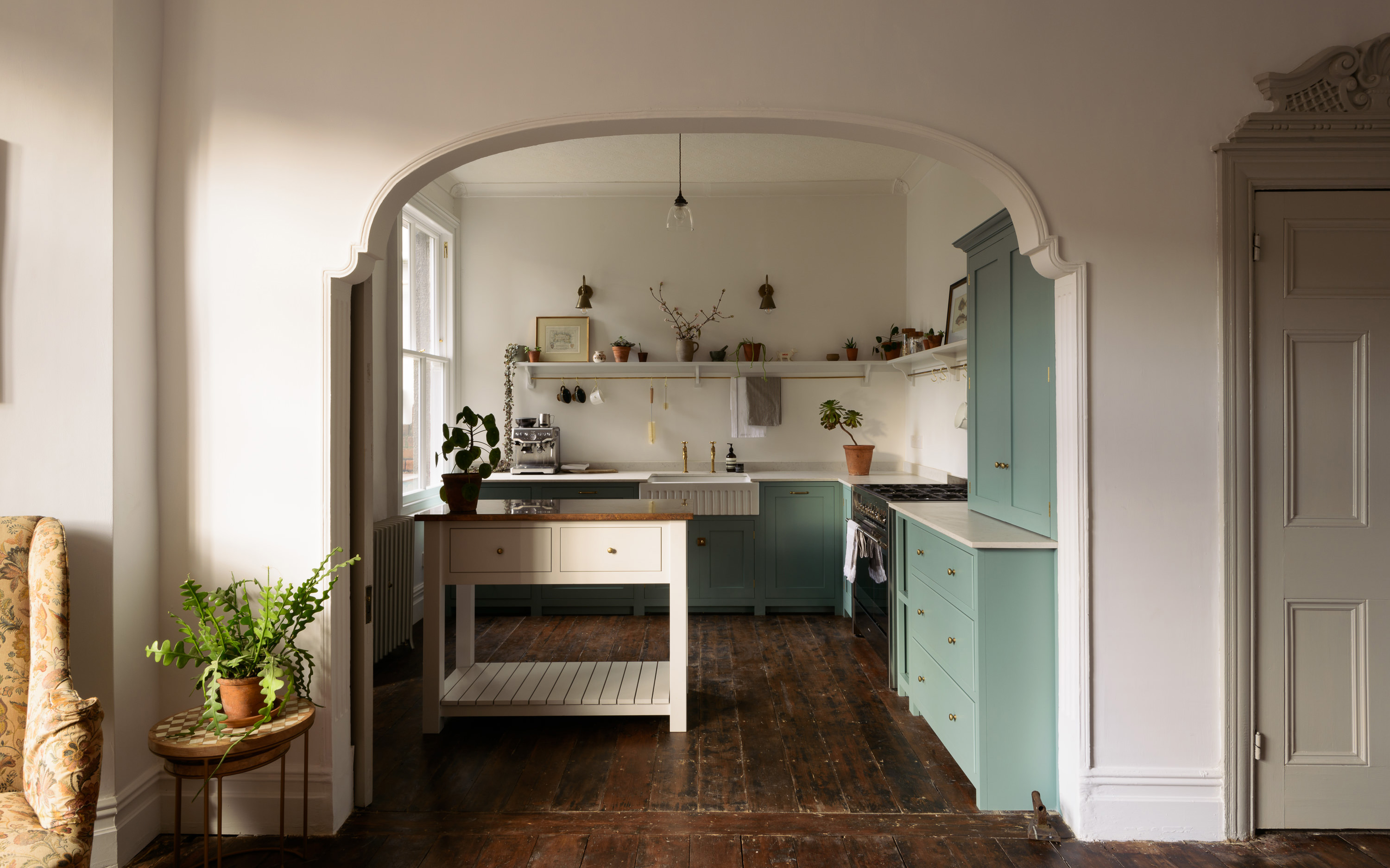 a small kitchen with a kitchen island and mint green cabinetry seen through a doorless archway with dark wooden floors
