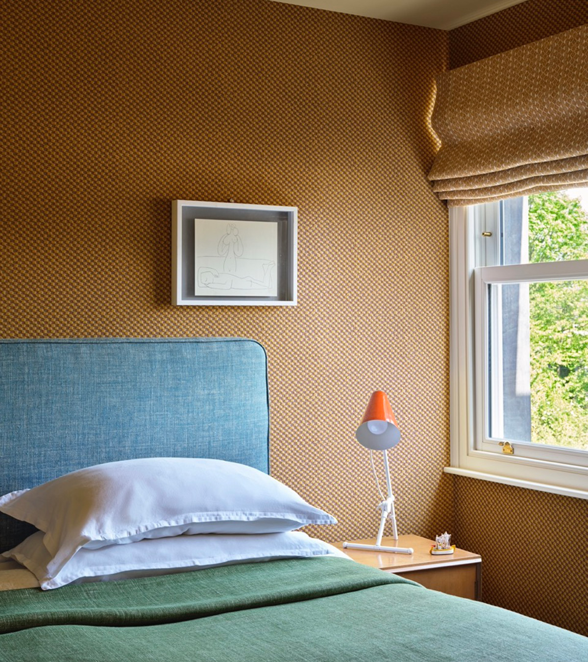 a bedroom corner with ochre yellow textured wallpaper, a bed with a blue headboard and a green bed spread
