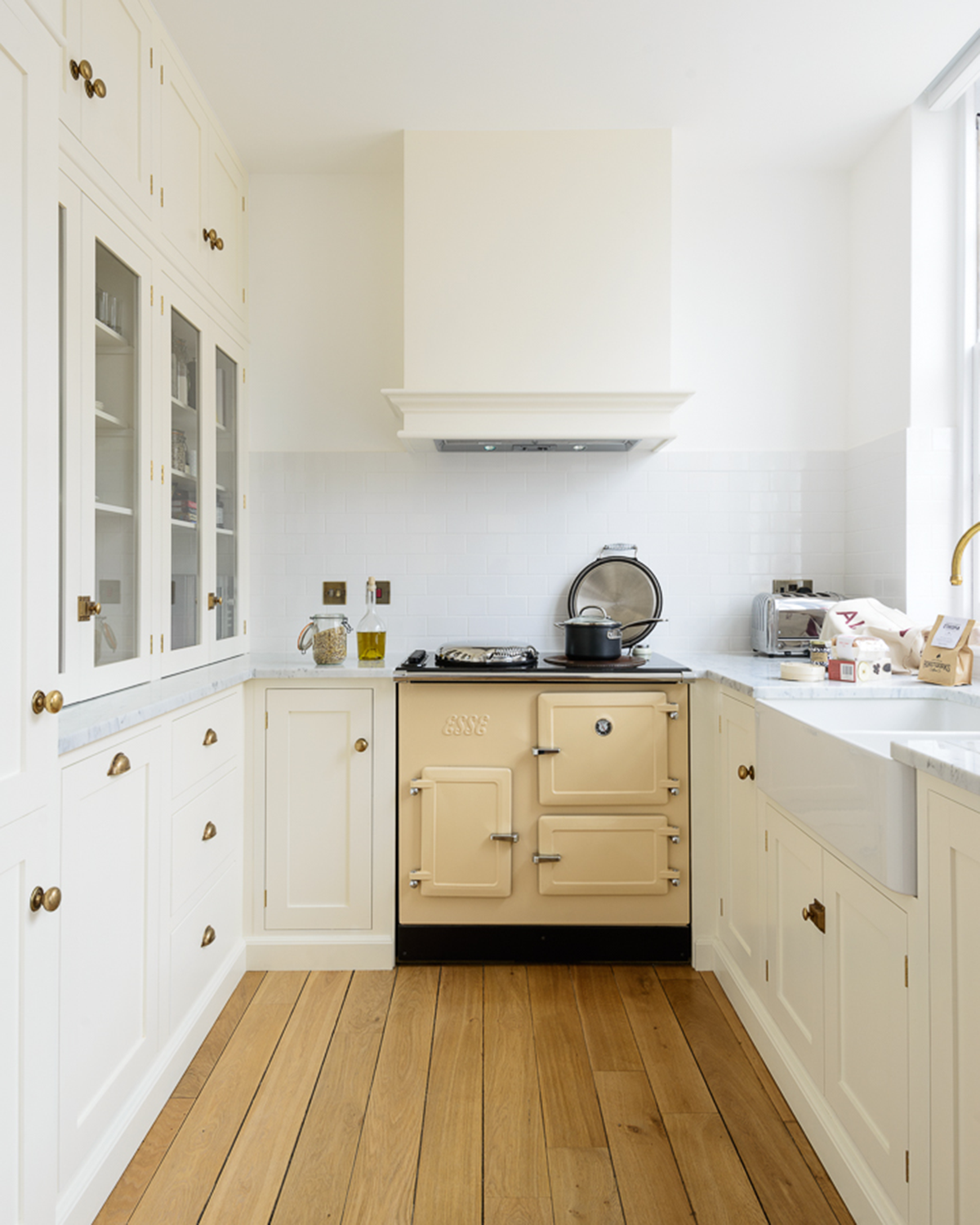 an all white kitchen with white cabinets, white tile splashback and white walls and a wooden floor and a pale yellow range cooker