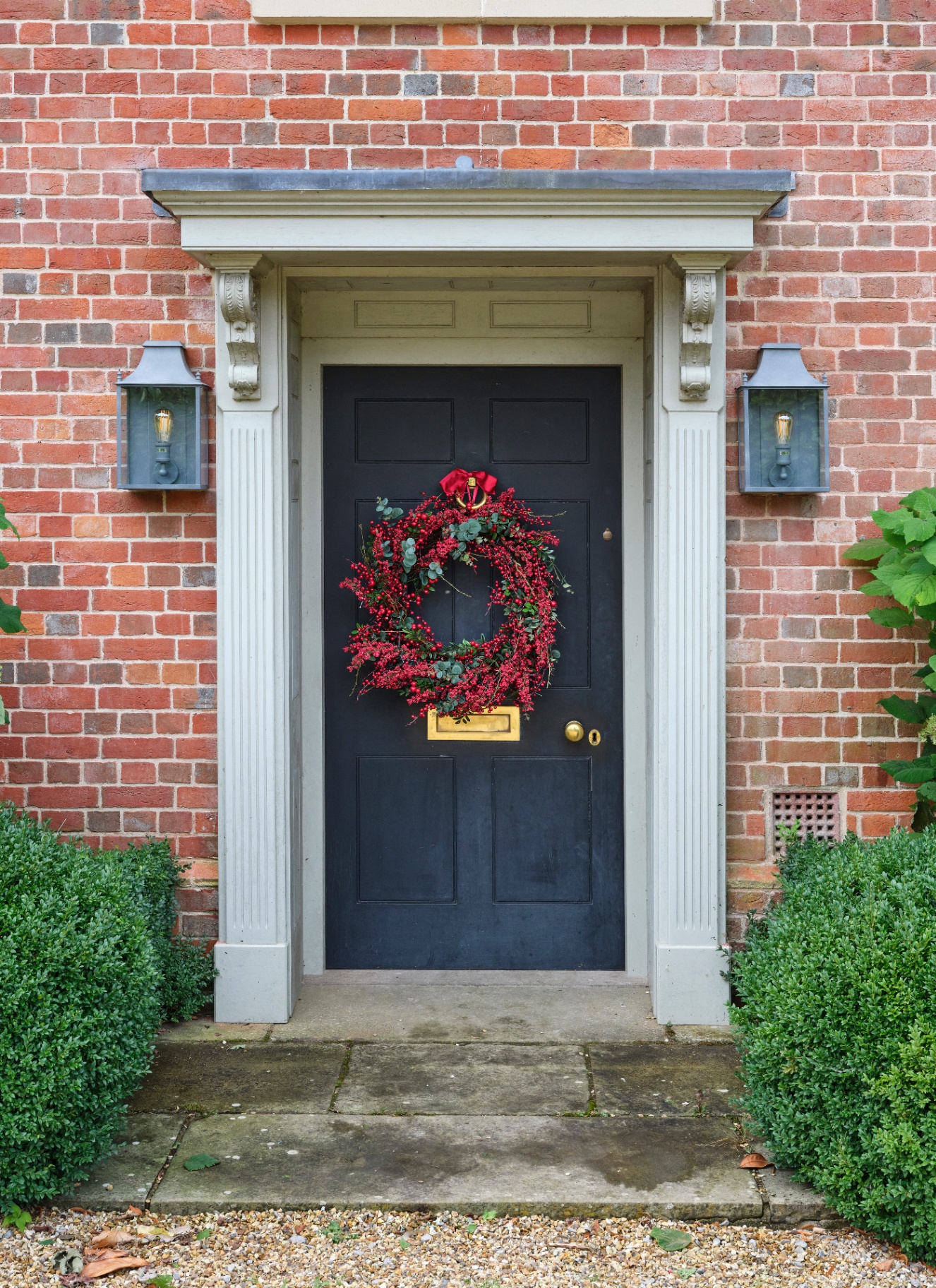 A dark front door adorned with a full red berry and eucalyptus Christmas wreath tied with a red ribbon.