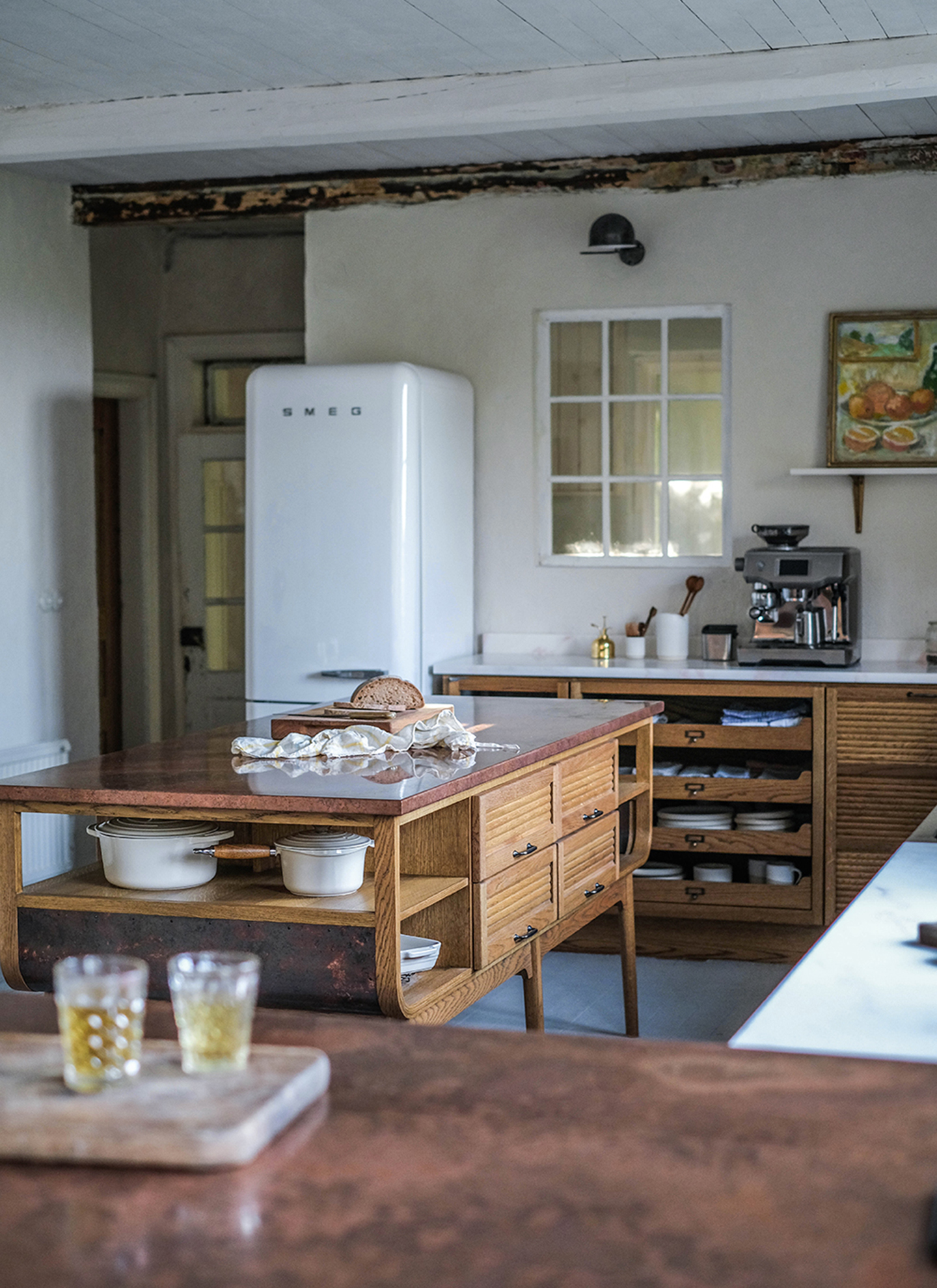 close up of a kitchen counter with pale pink cabinetry and marble tops, a silver coffee machine and a white gluggle jug