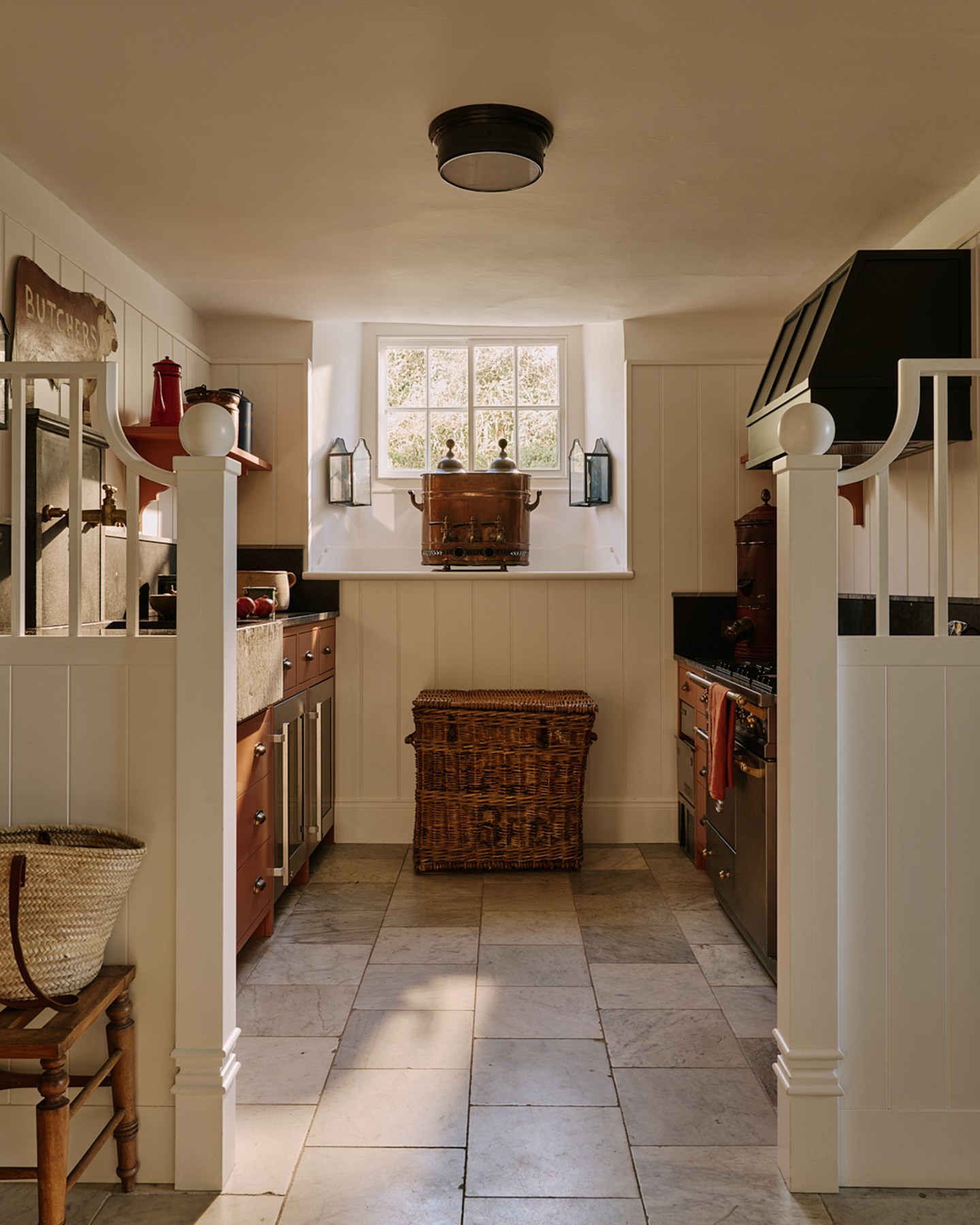 a country kitchen with cream honed marble floors, rust orange kitchen cabinets and a large wicker basket under the window