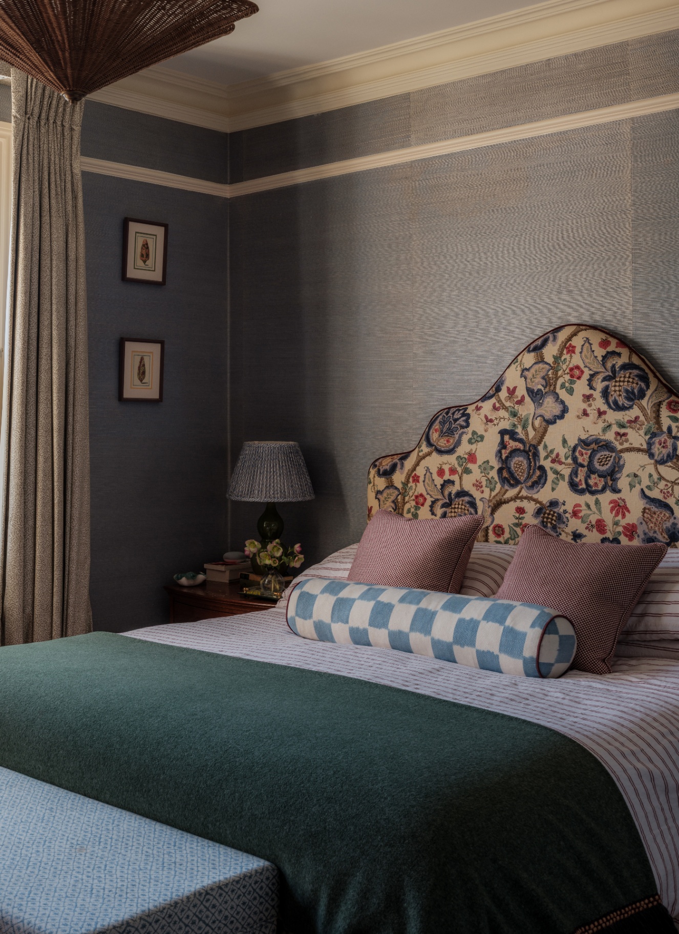 A cosy bedroom with blue wallpaper, featuring a small bedside table lamp with a dark pleated fabric shade on a wooden nightstand