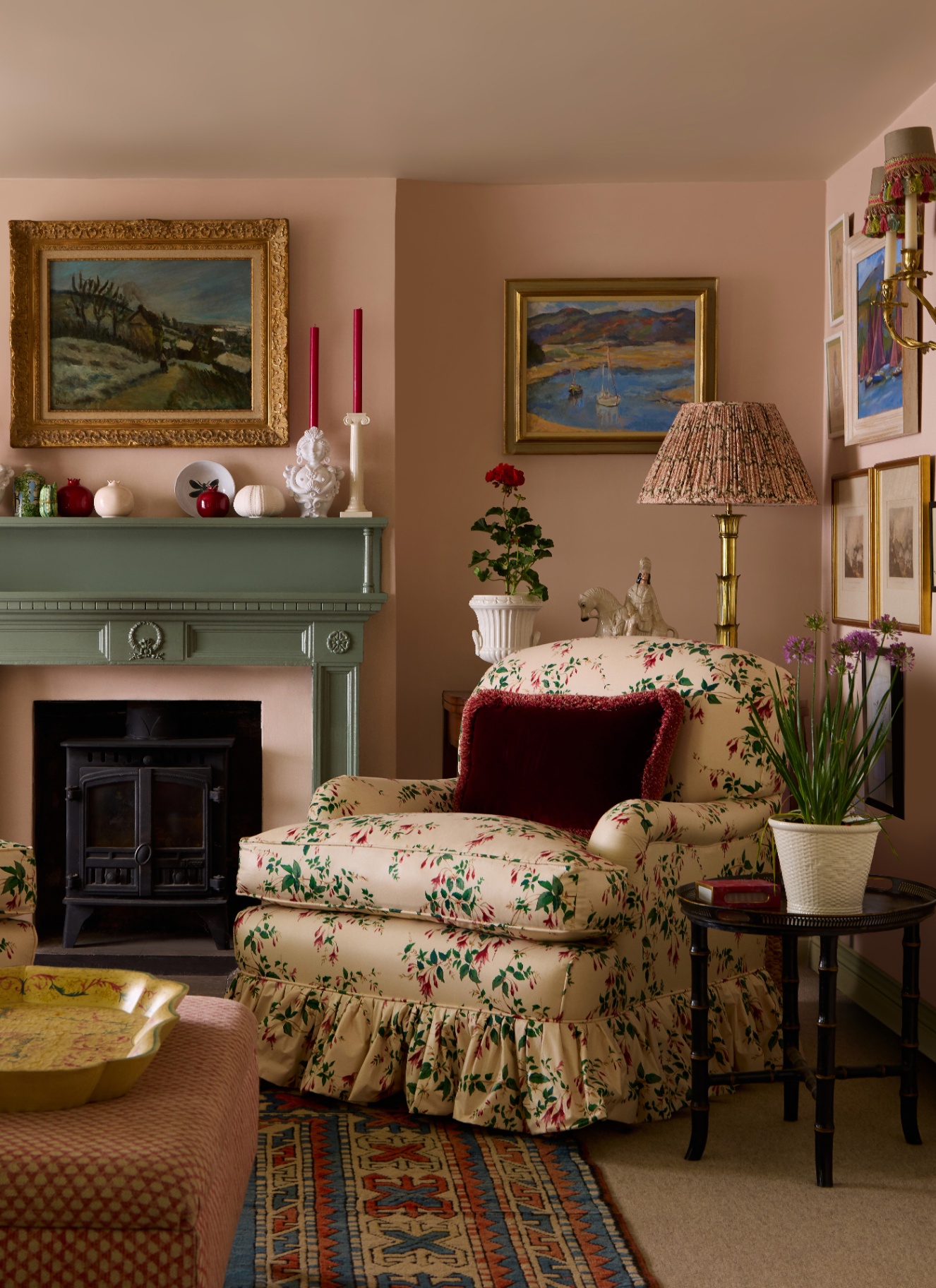 a sitting room with plaster pink walls, a green painted fireplace and a cream and green botanical printed skirted armchair