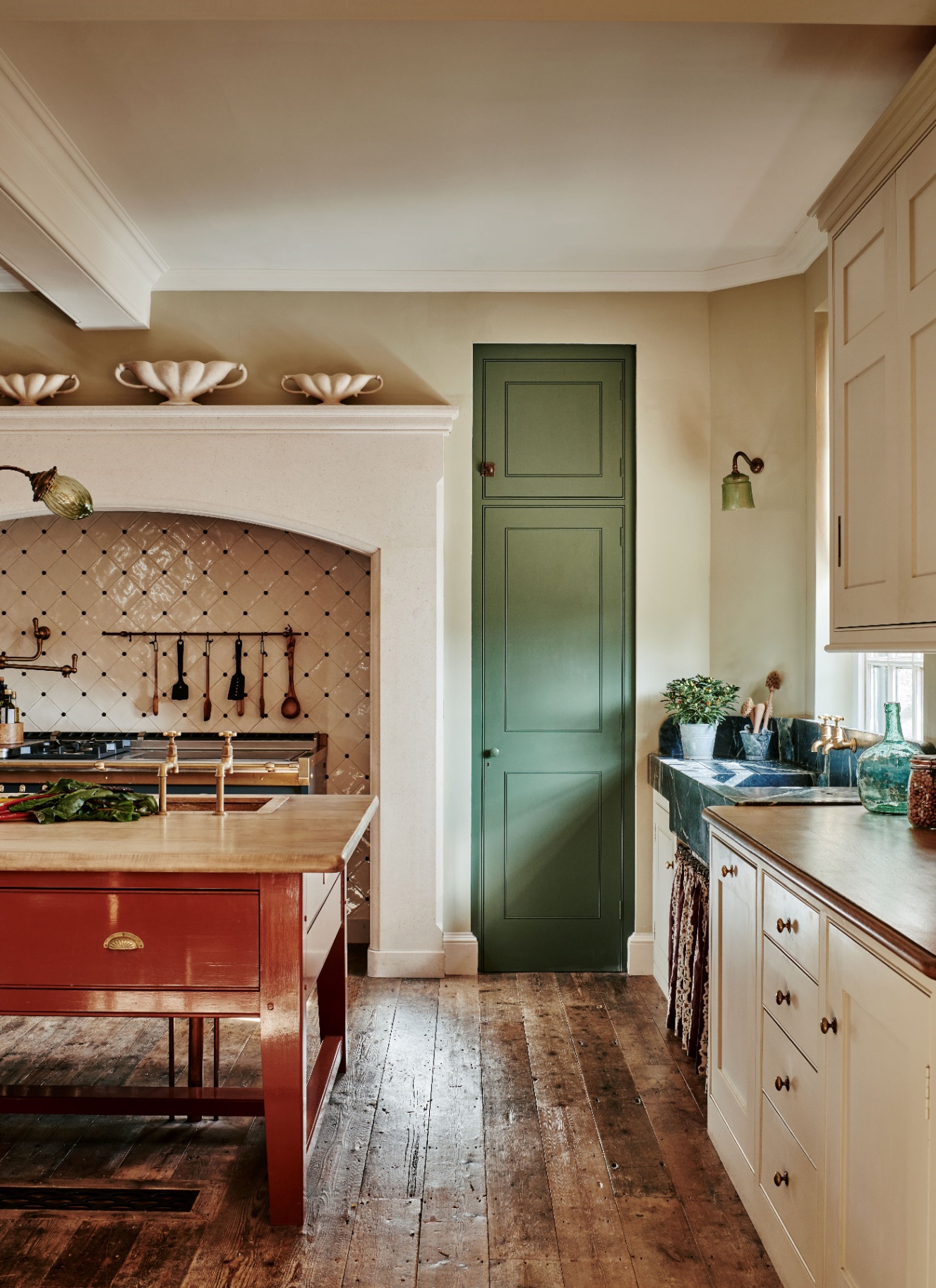 a kitchen with a red kitchen island, woode floors, white cabinetry, a green door and a tiled splashback behind cooker