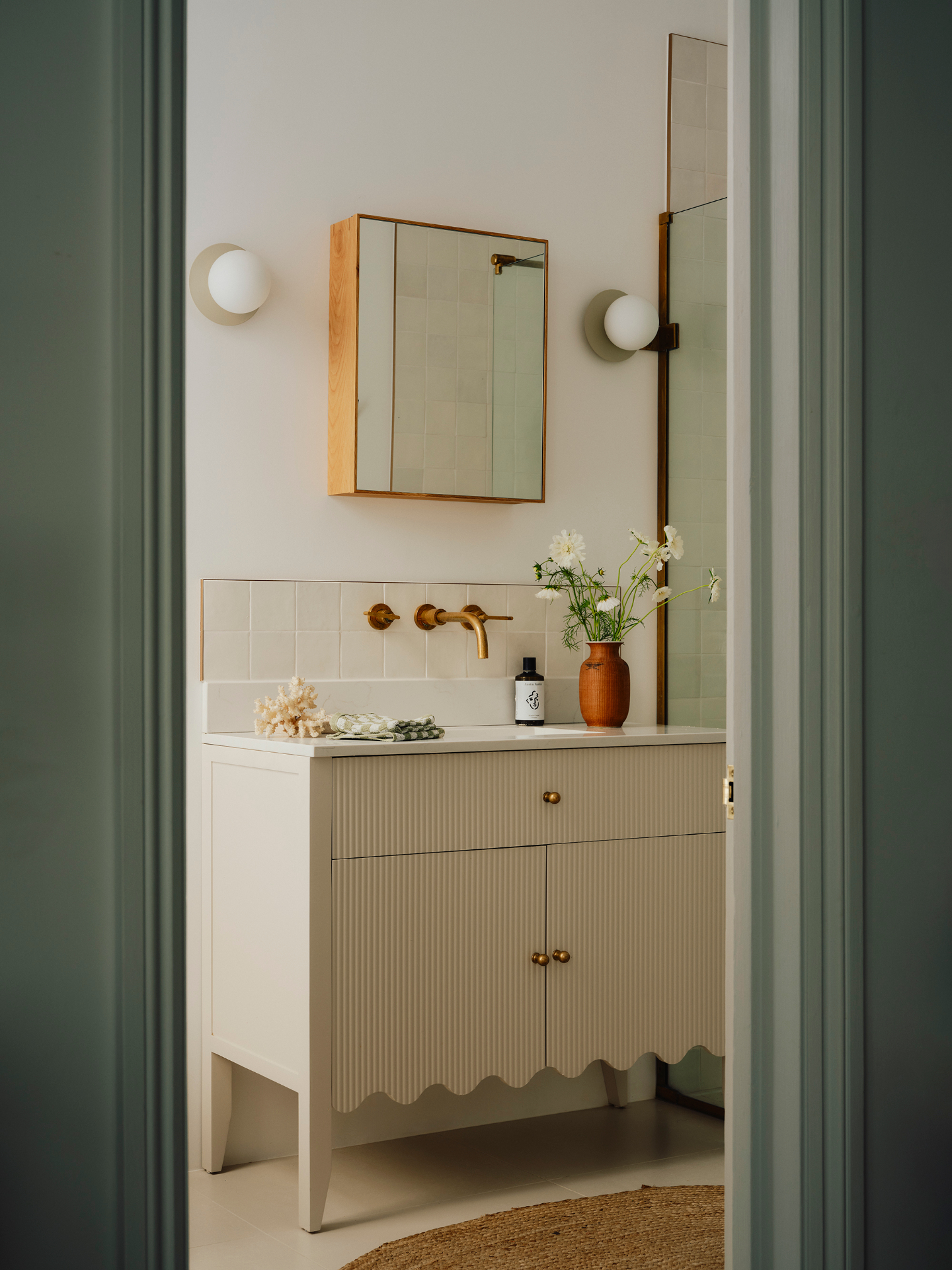 a bathroom pictured with a statement scalloped wood vanity at the centre with a mirror and flowers 