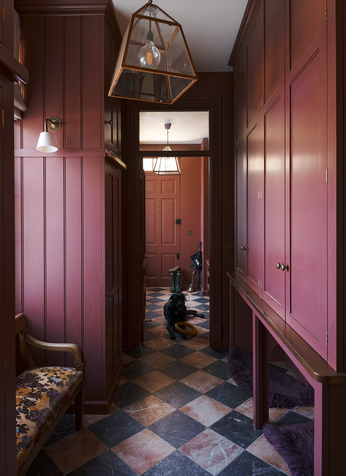 a dark red panelled boot room with a brown and blak checkered tiled floor and a black labrodor laying on the floor