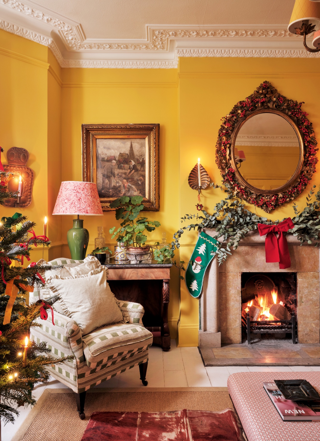 An ochre sitting room featuring a fireplace garland tied with a large red velvet ribbon and a matching wreath over an ornate mirror