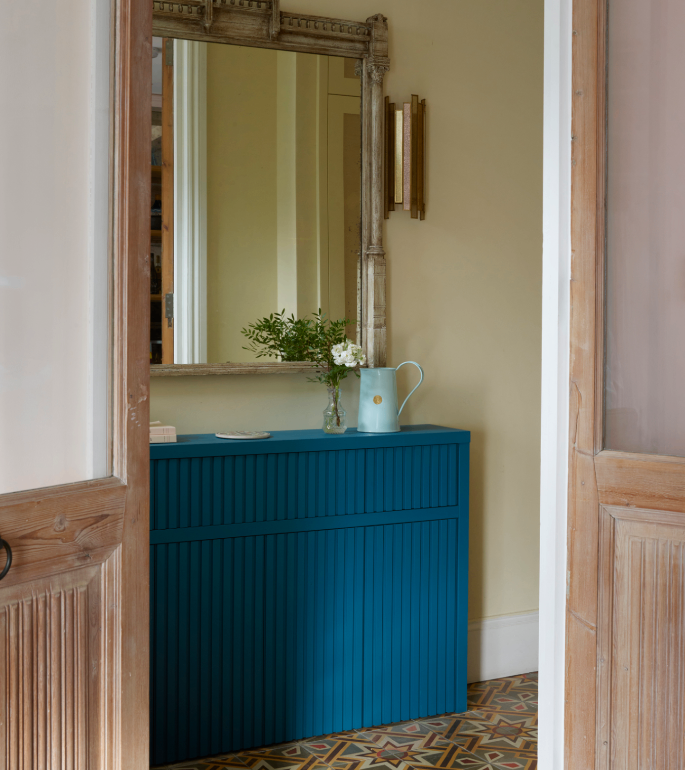 a hallway with a large mirror above a teal blue painted radiator cover