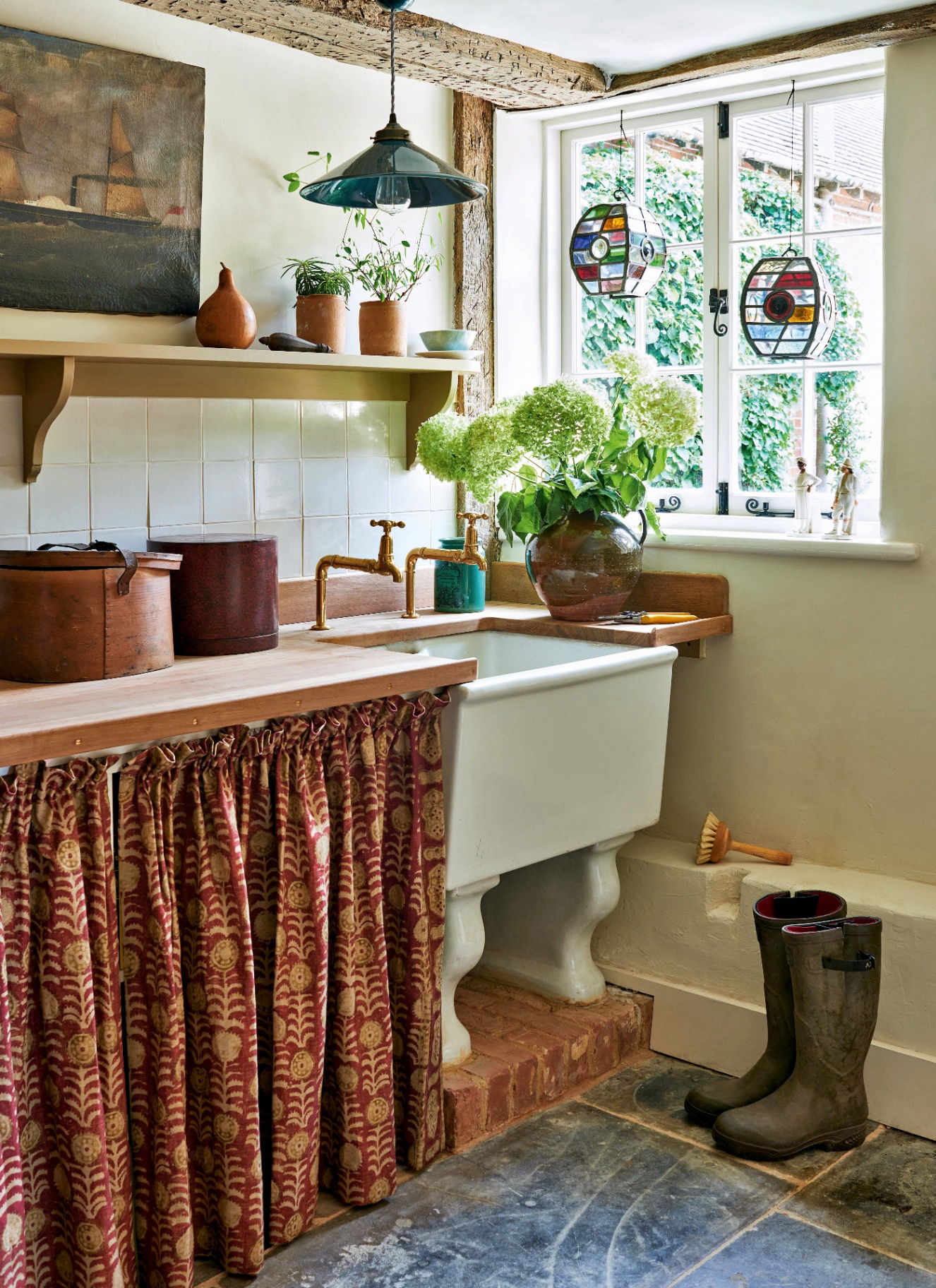 a utility room with a large belfast sink, a red botanical patterned sink skirt and an open shelf with terracotta pots