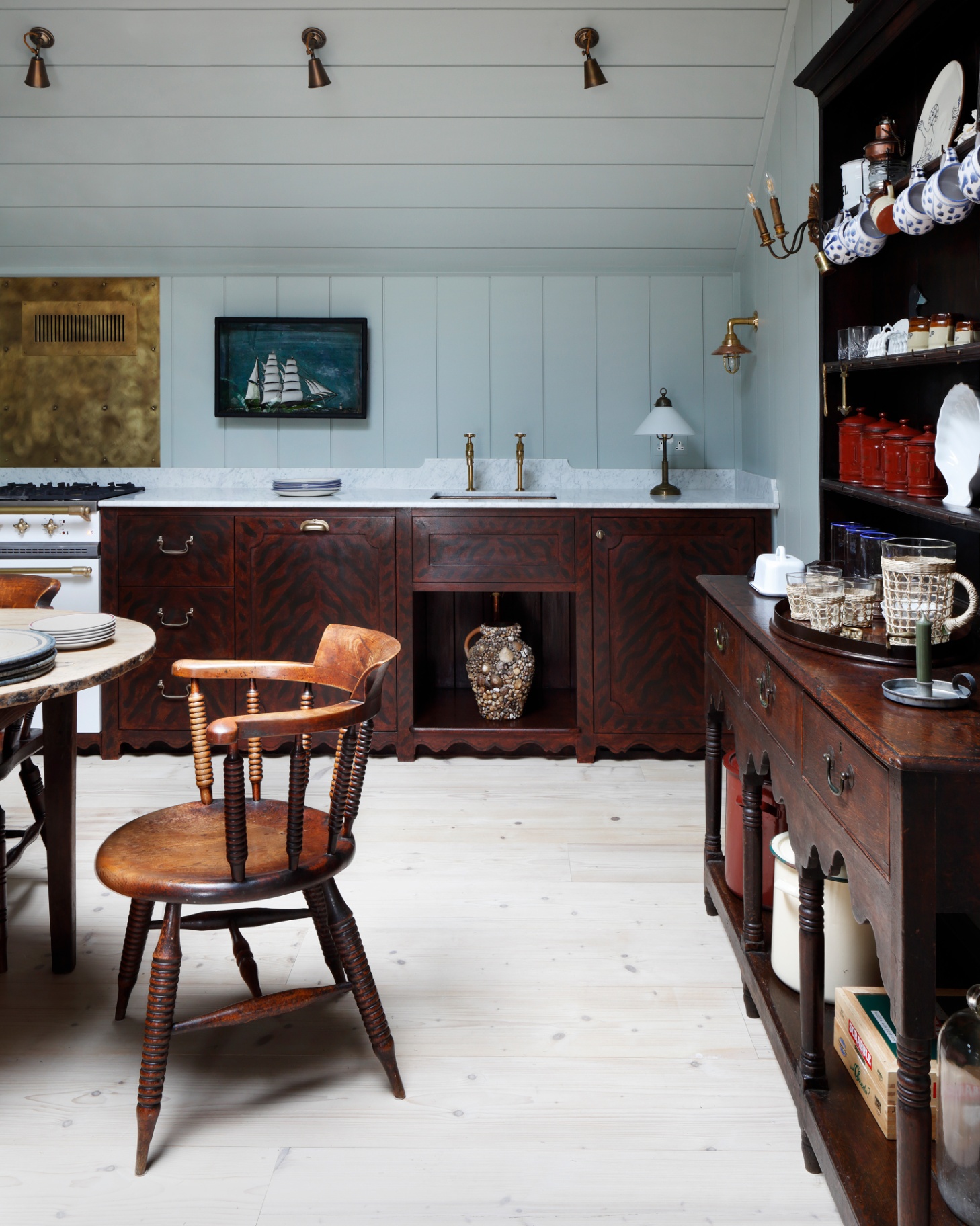 a kitchen with dark wooden cabinetry, a large antique dresser to the right filled with plates and an antique dining chair