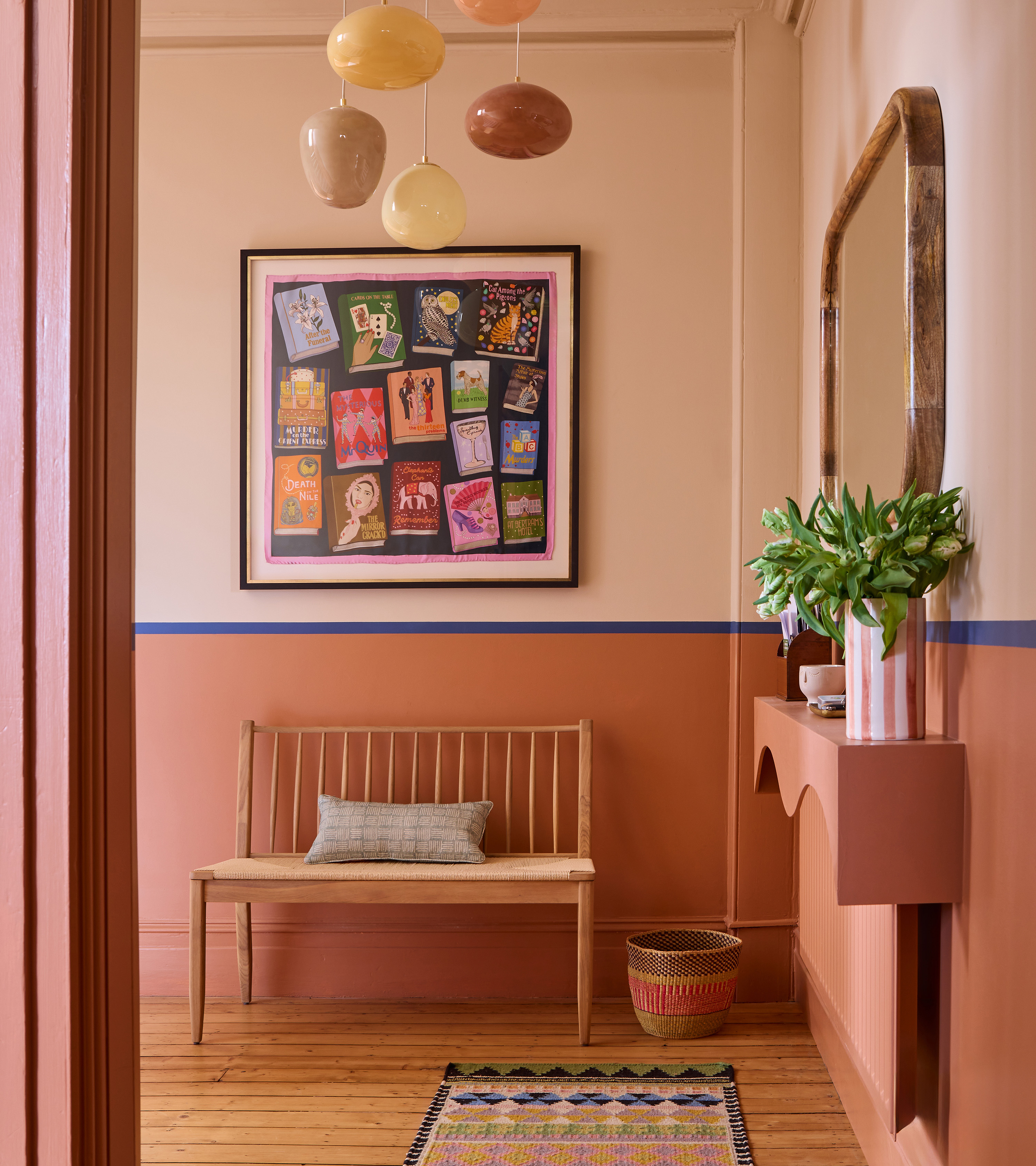a two tone pink hallway with a blue border halfway up the wall, a irregular circle neutral pendant, a large artwork above a cane bench