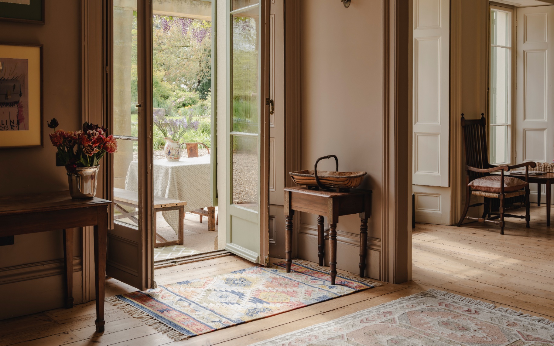 a hallway with wooden floors, patterned jute rugs, open doors looking out to a conservatory and a wooden console table with a vase of flowers