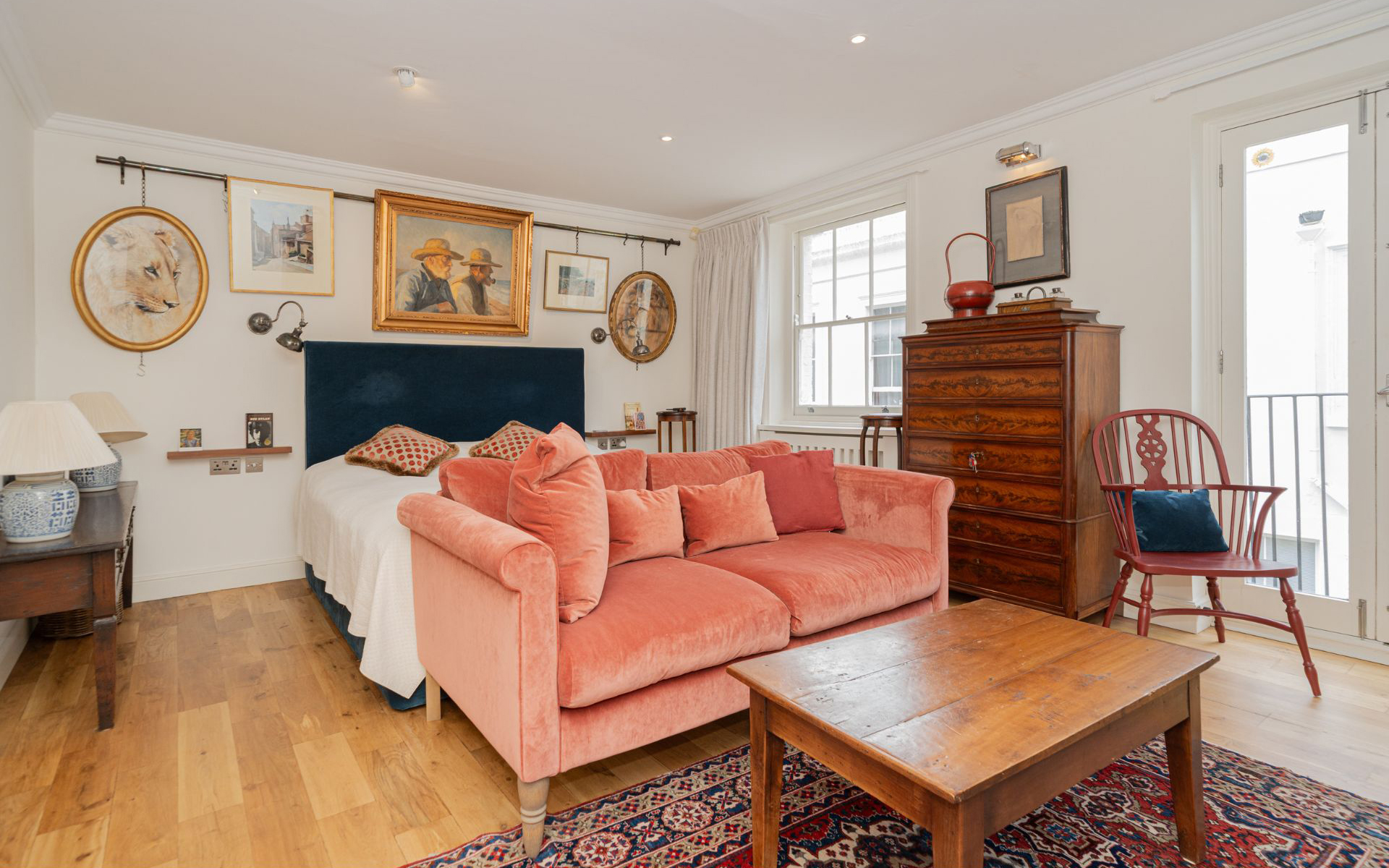 the bedroom of madonnas former london home, with a salmon pink sofa, a bed with a navy headboard, painting on the walls and a large wooden dresser