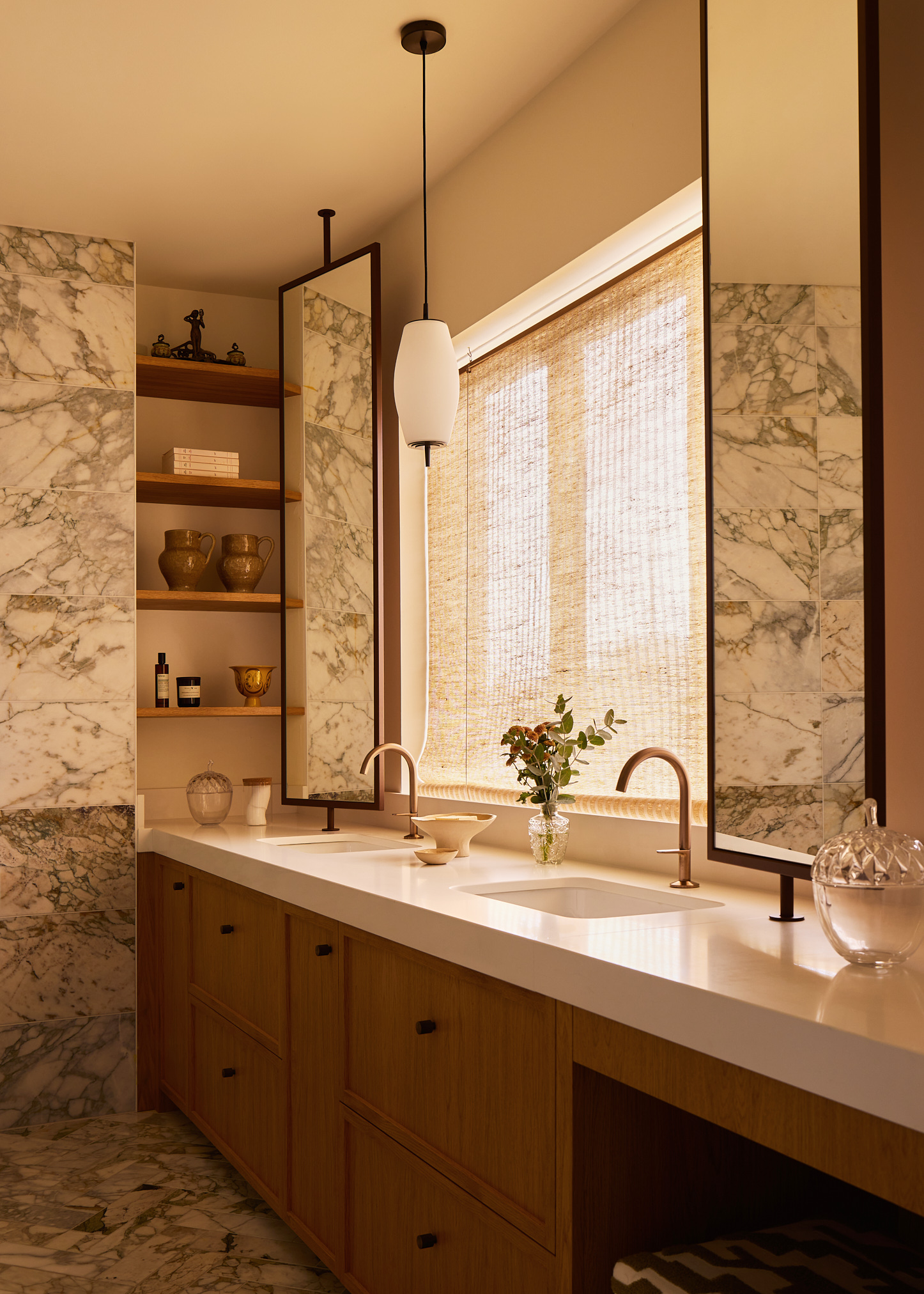 a dimly lit bathroom pictured with marble walls and wooden accents and brass fixtures