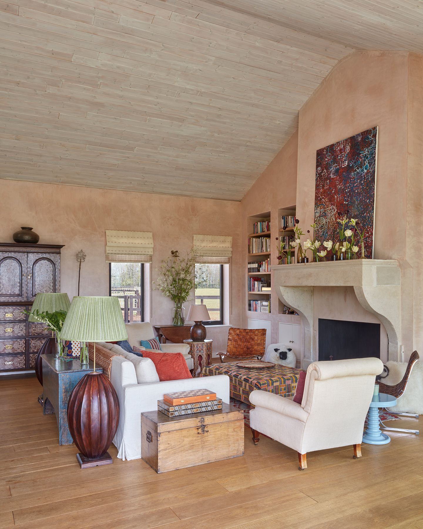 A white sofa and cream armchairs surround an ottoman covered in an african cloth. The tall ceilings are clad with timber and the walls are raw plaster. A mix of lacquer side tables, vintage chests and consoles are arranged with two large floor lamps
